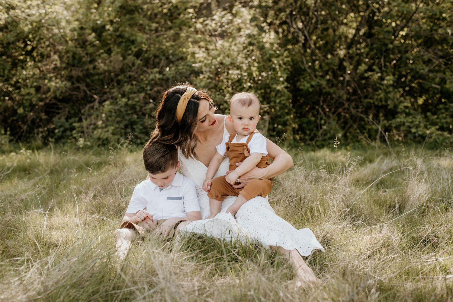 Mother and children relaxing together in a sunny meadow with tall grass.