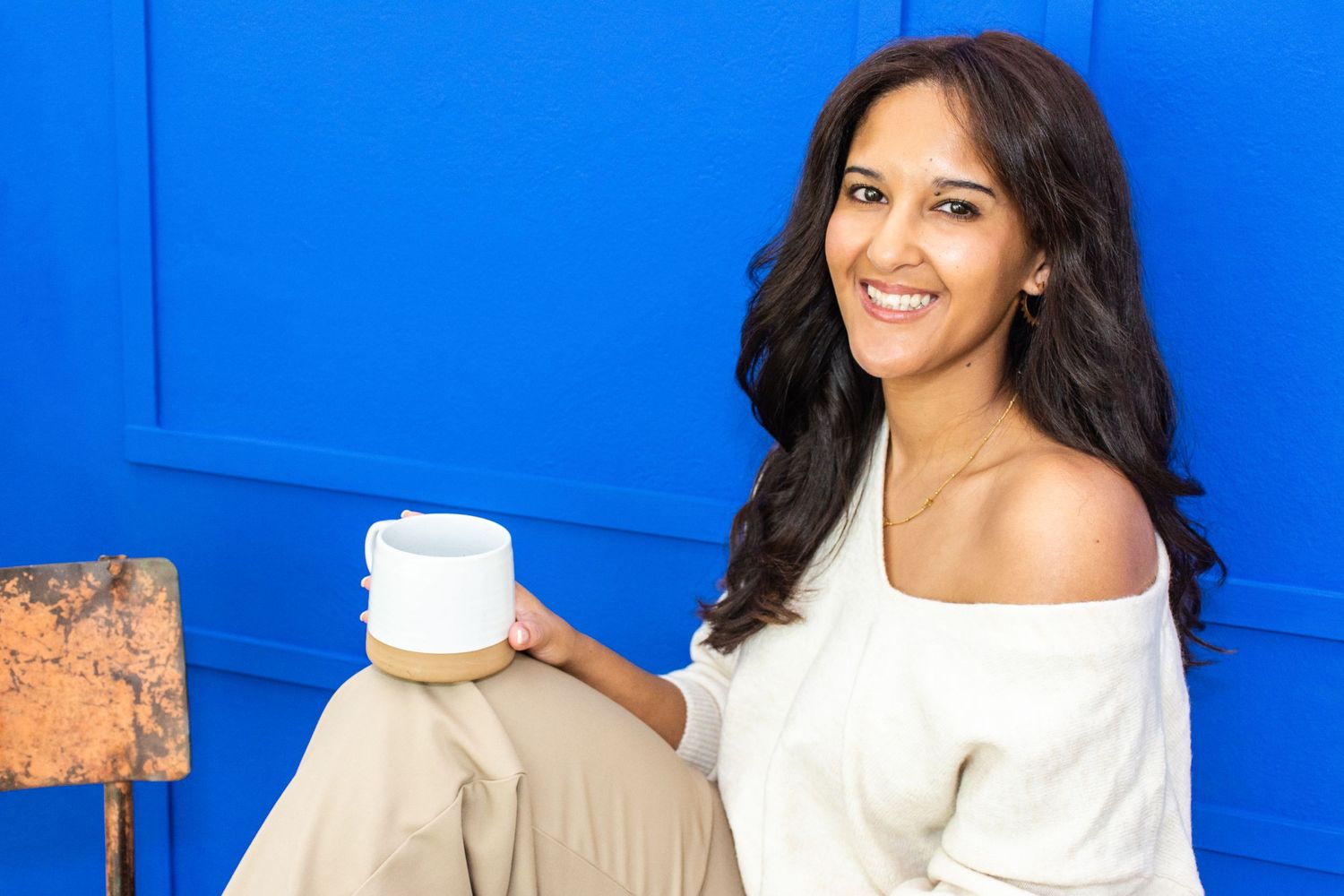 Coach with coffee mug sitting in front of blue wall