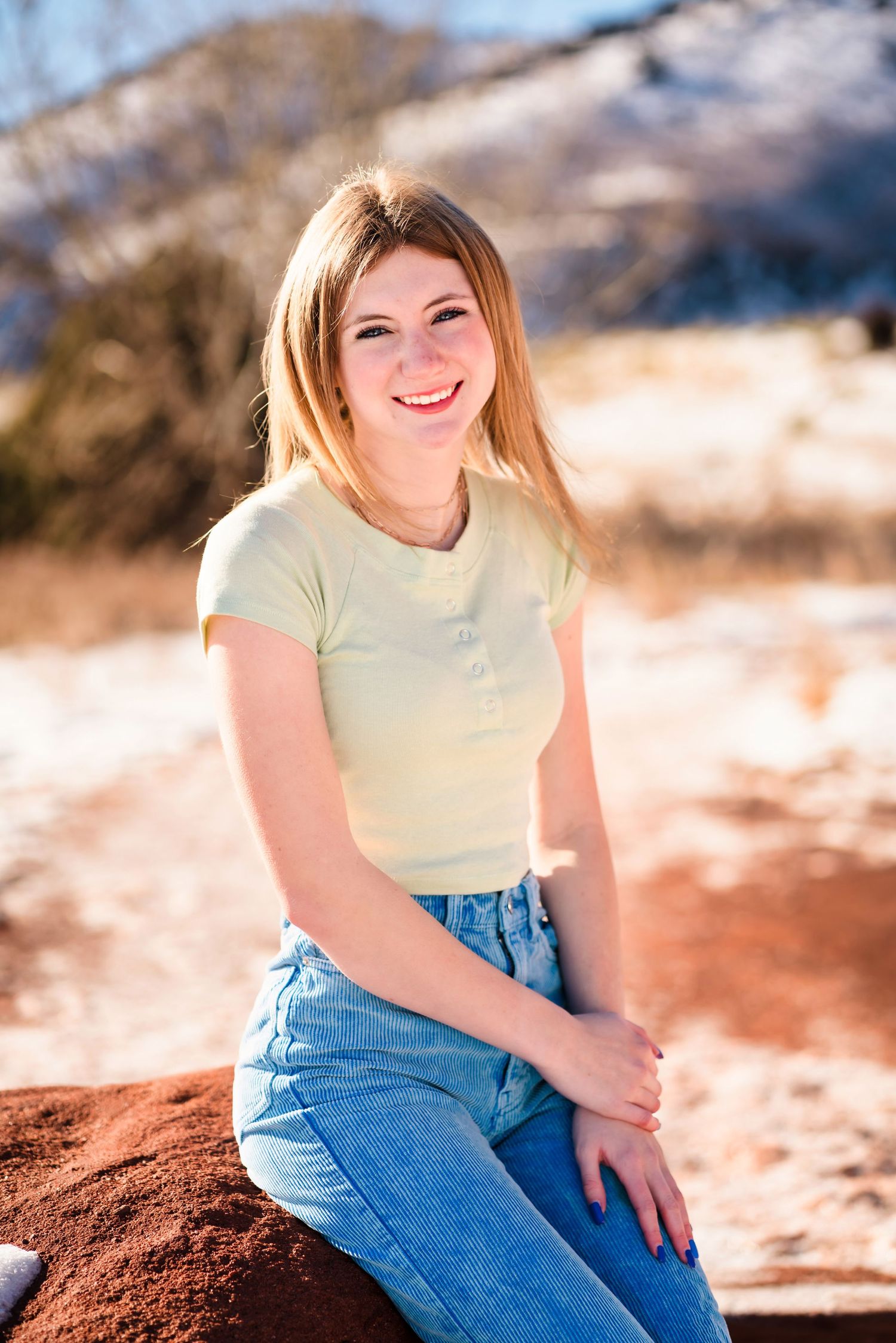 Casual outdoor portrait with yellow shirt and jeans against snowy mountain backdrop.