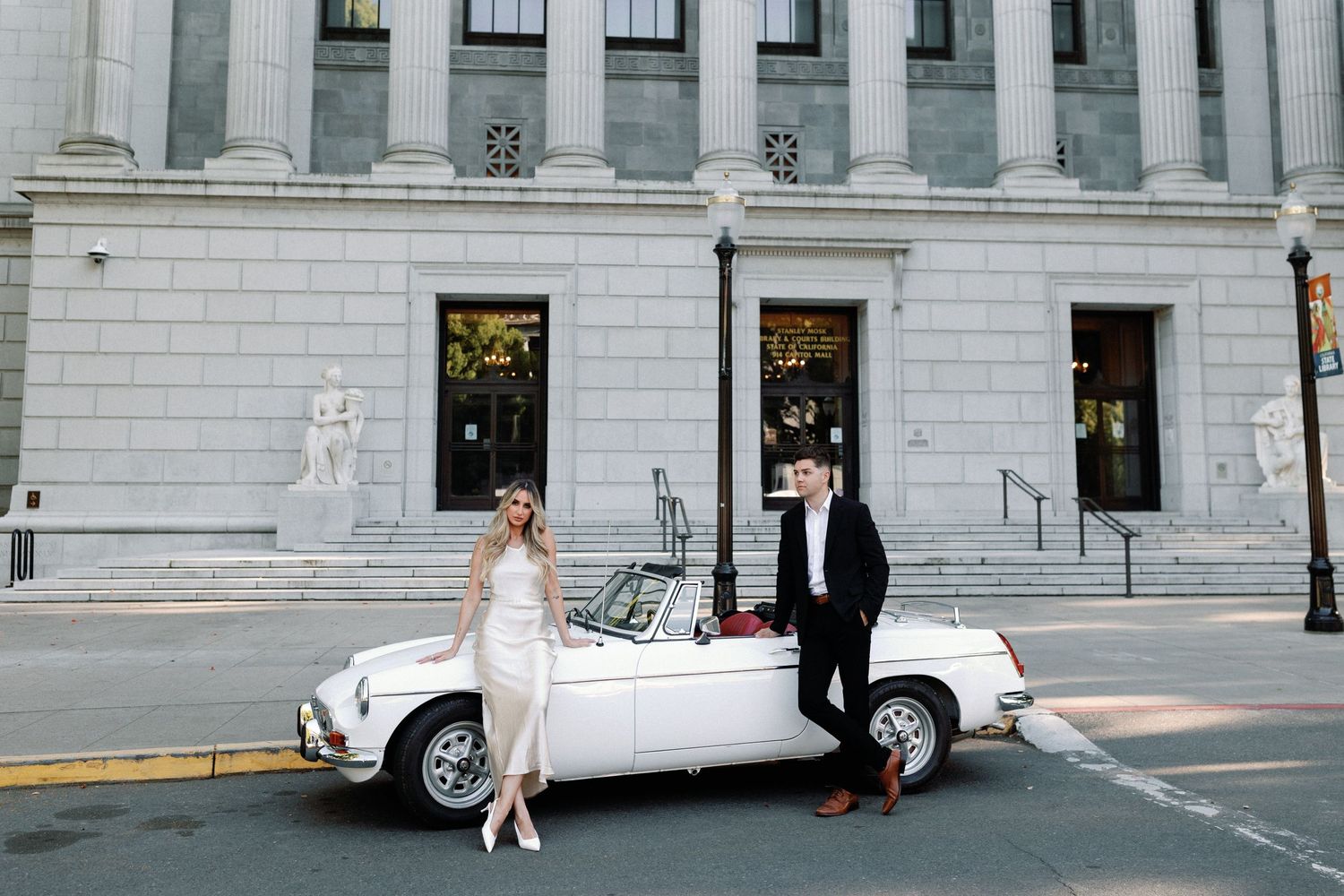 A classic white convertible car parked in front of an elegant stone building with columns.