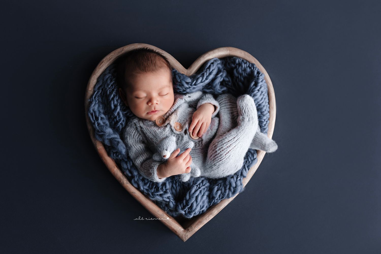 A sleeping newborn in cozy knit fabrics rests in a wooden heart-shaped container.