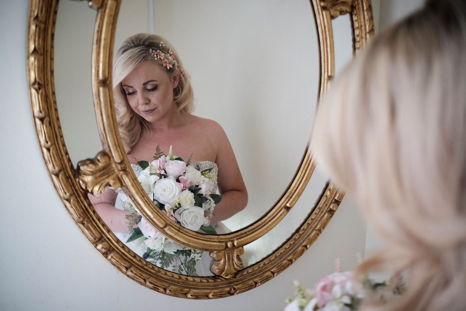 A bridal reflection captured in an ornate gold mirror with floral bouquet.