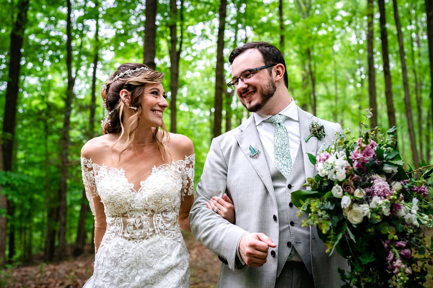 Wedding couple poses in lush green forest setting with floral decorations.