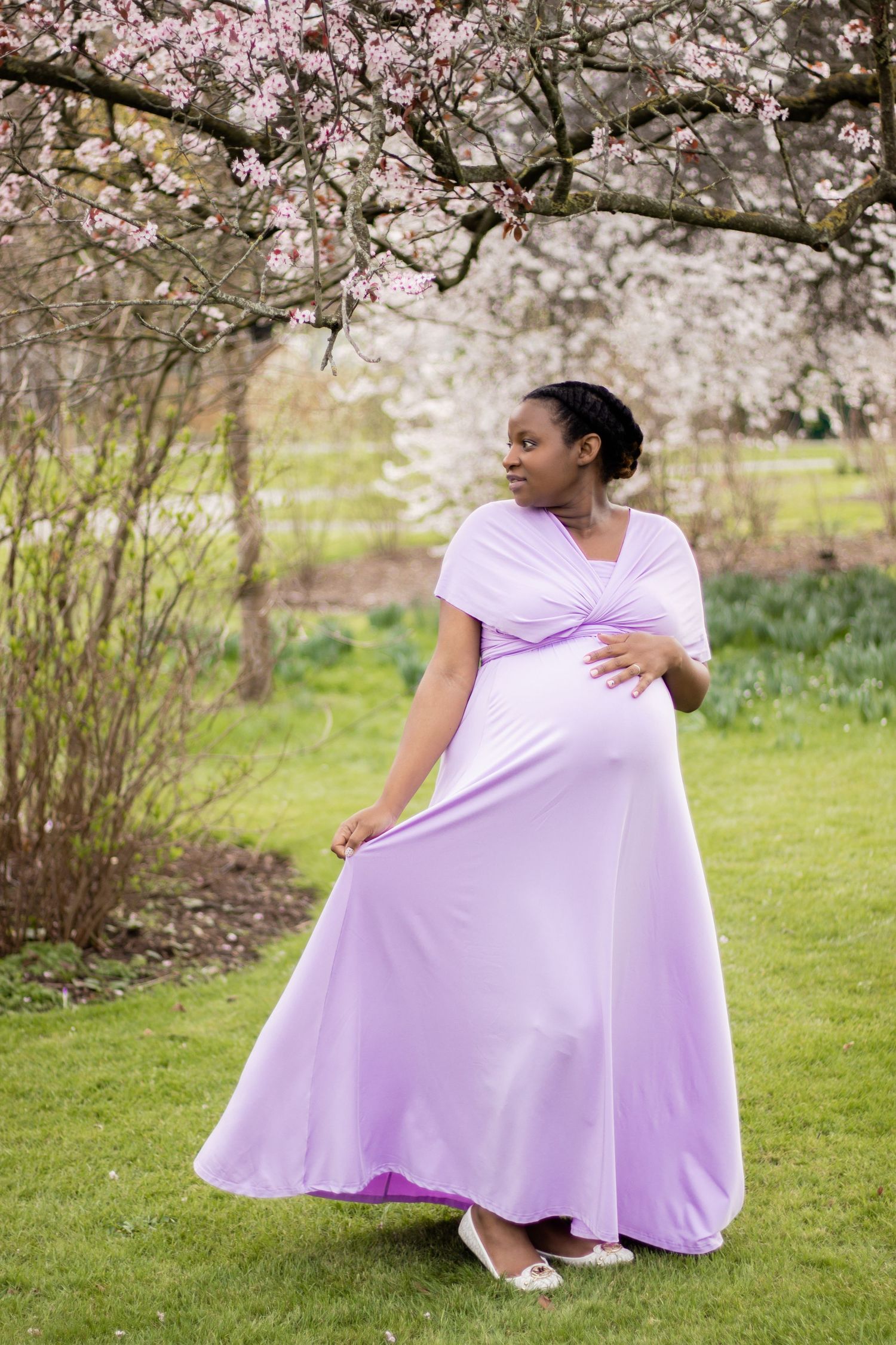 Spring maternity portrait in flowing lilac dress under blooming cherry trees.