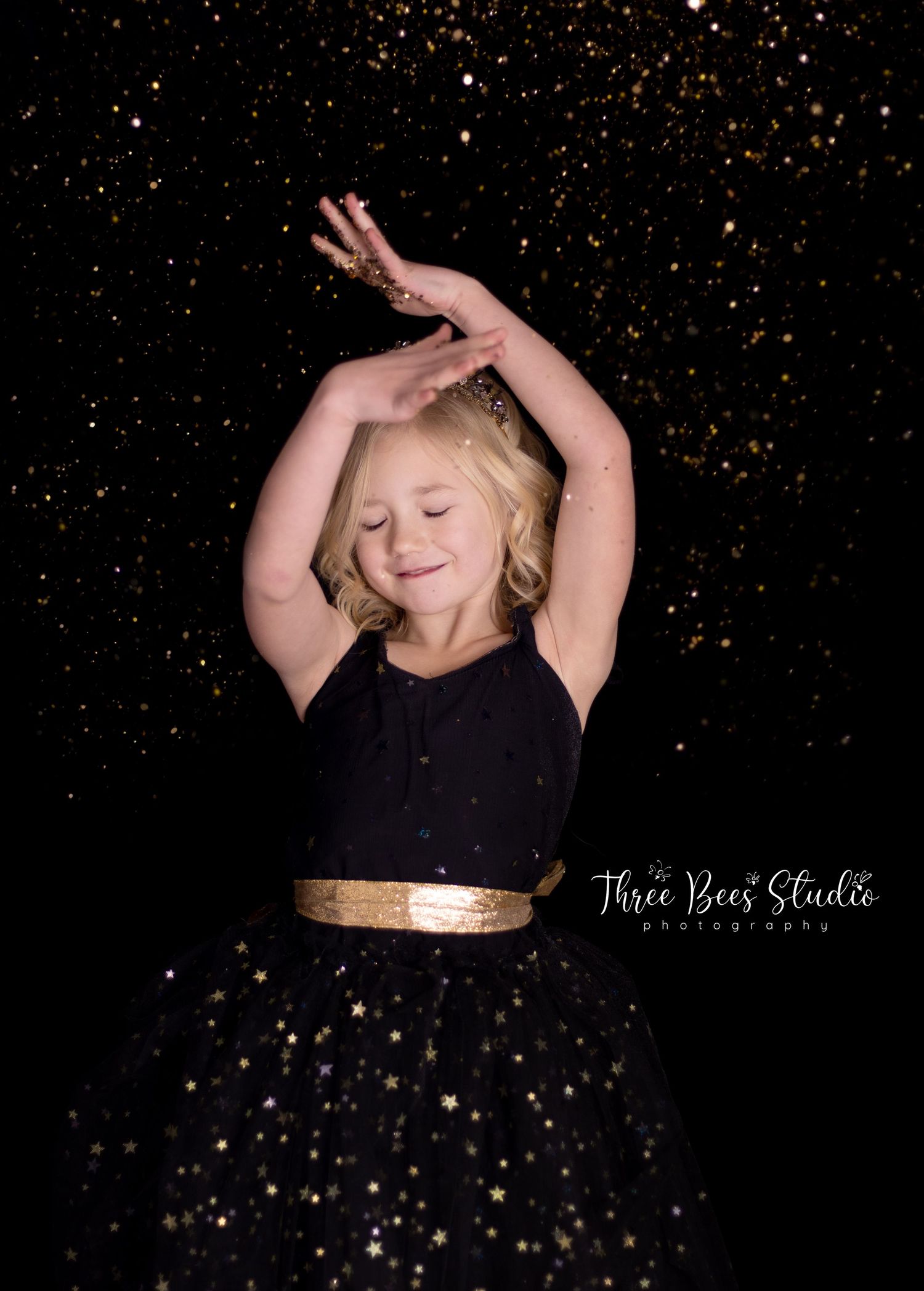 Dance pose in black and gold dress against sparkling dark backdrop.