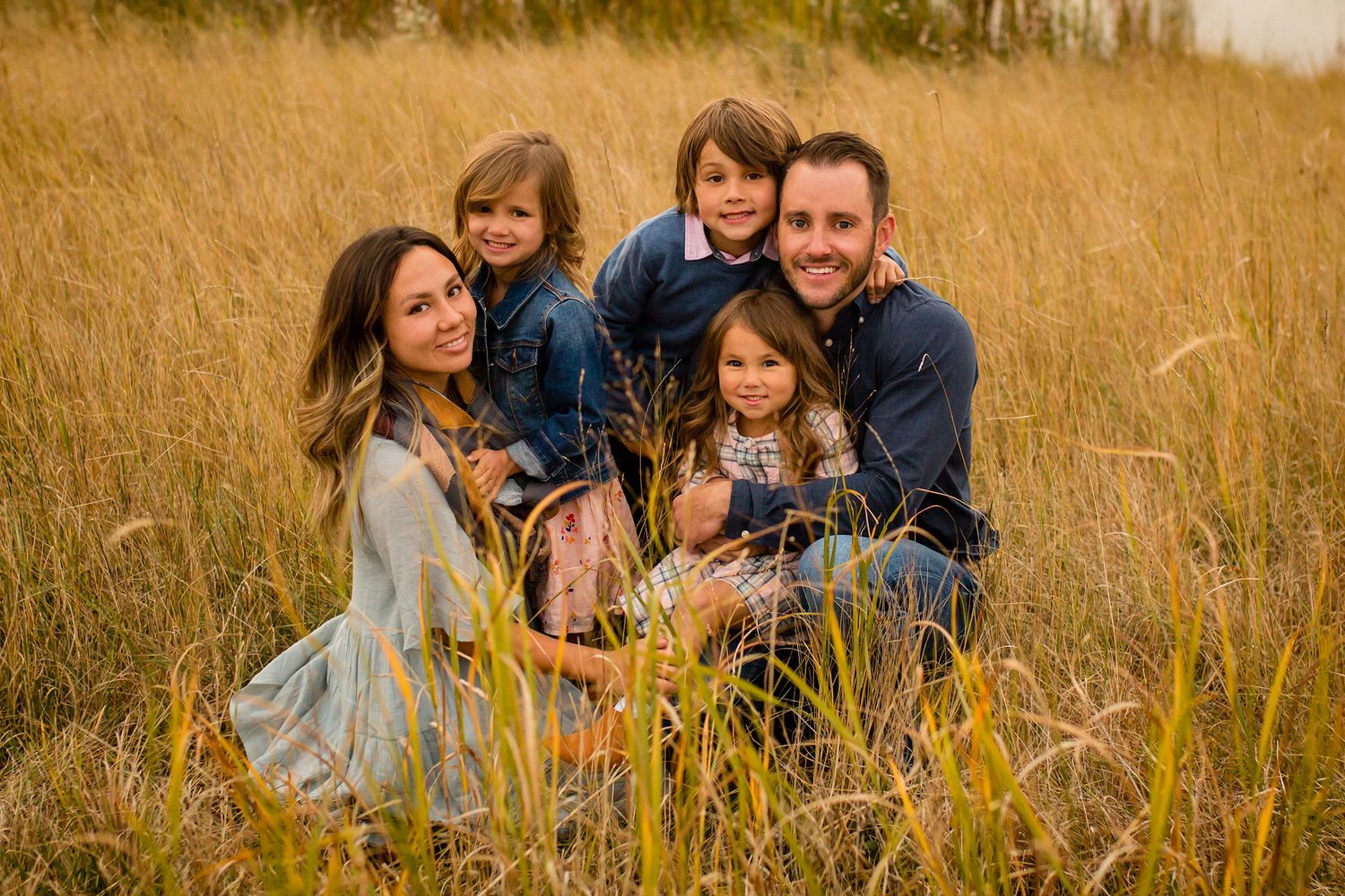 Family group lounging together in tall golden grass during sunset photo session.