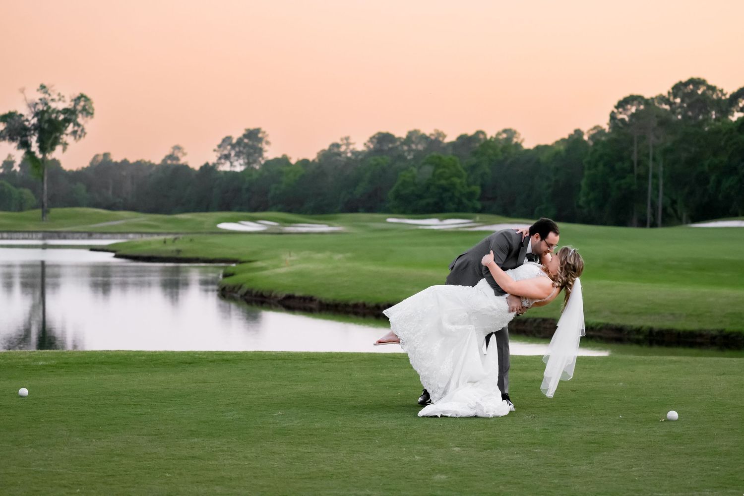 Romantic wedding photo of newlyweds on a golf course at sunset near a water hazard.