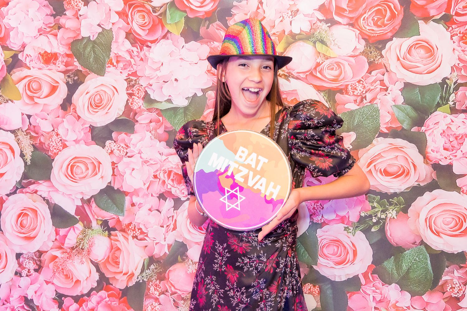 A floral backdrop with pink roses frames someone holding a circular sign.