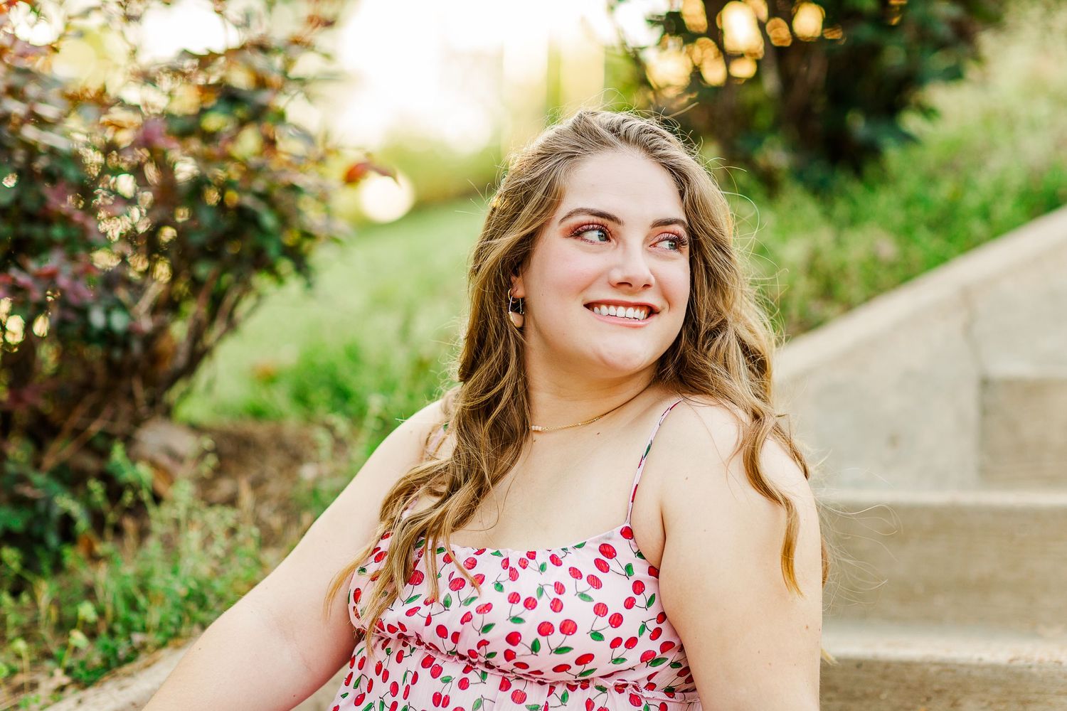 Outdoor portrait of a person in a red floral dress sitting on steps during golden hour.