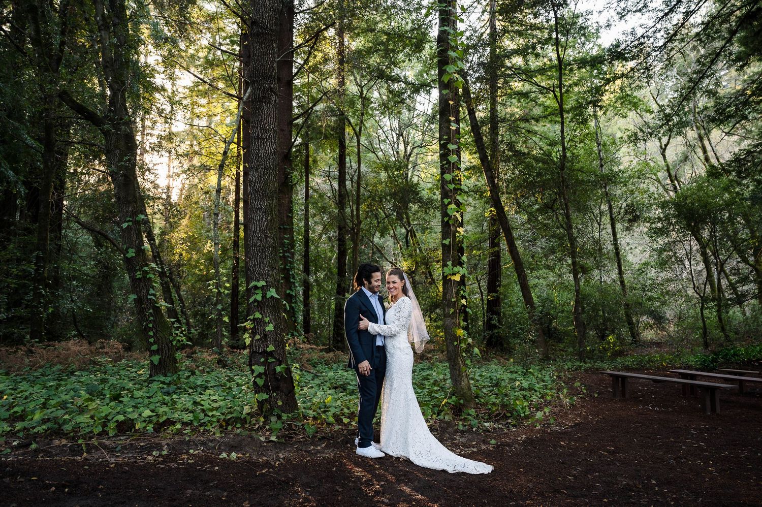 A couple poses for a wedding portrait on a misty forest path surrounded by tall evergreen trees.