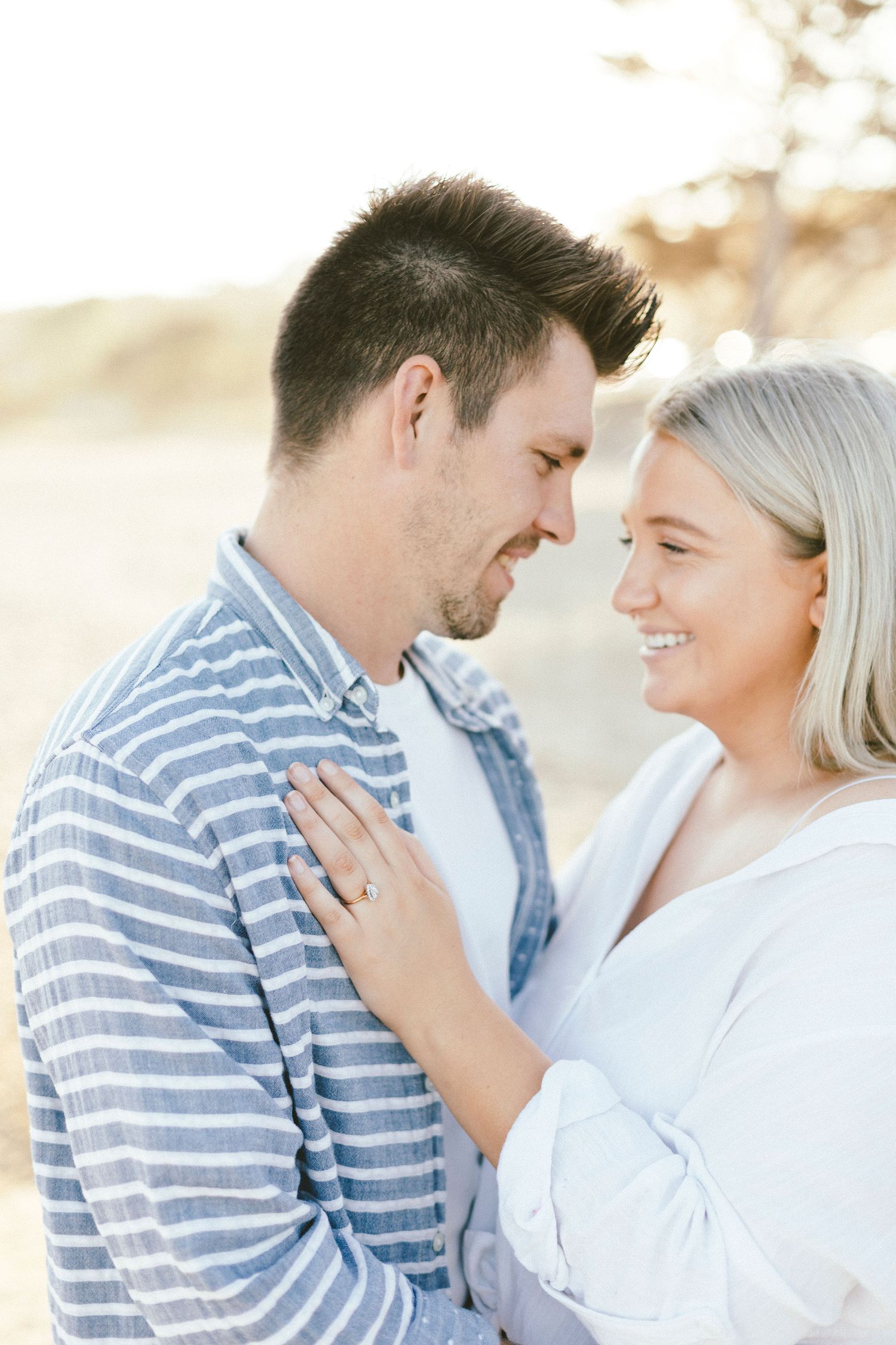 A couple in casual attire sharing a tender moment against a bright background.