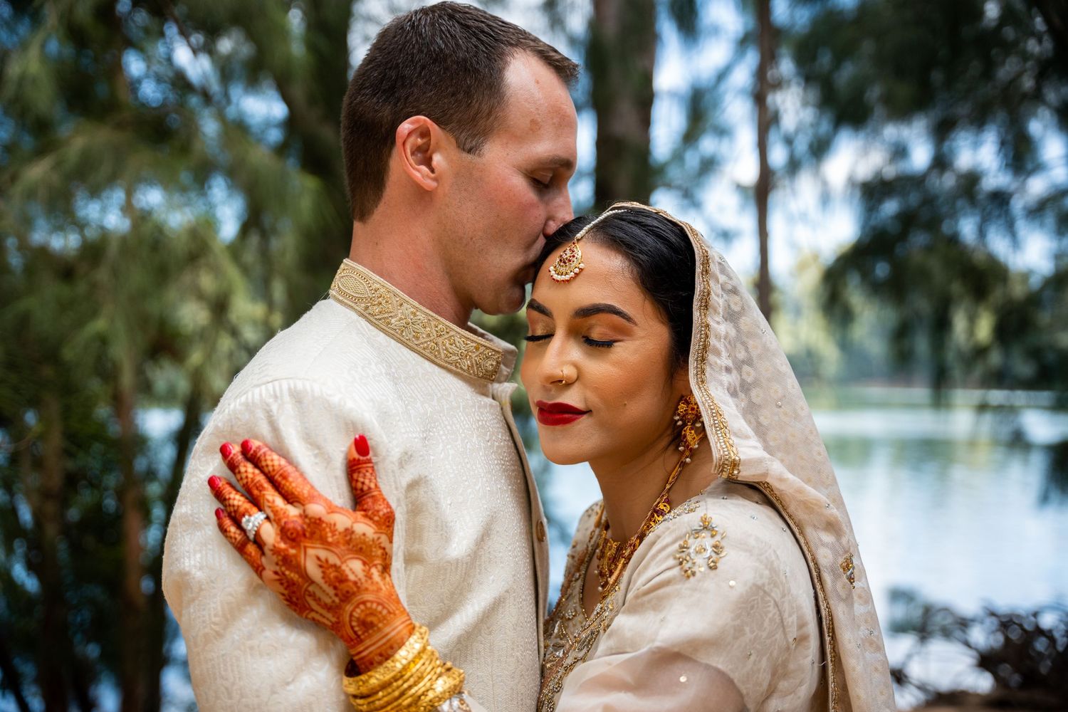 Traditional wedding couple in elegant white and gold attire sharing intimate moment.