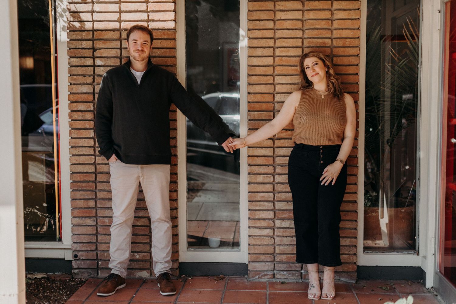 A couple stands playfully in a doorway with wooden shutters.