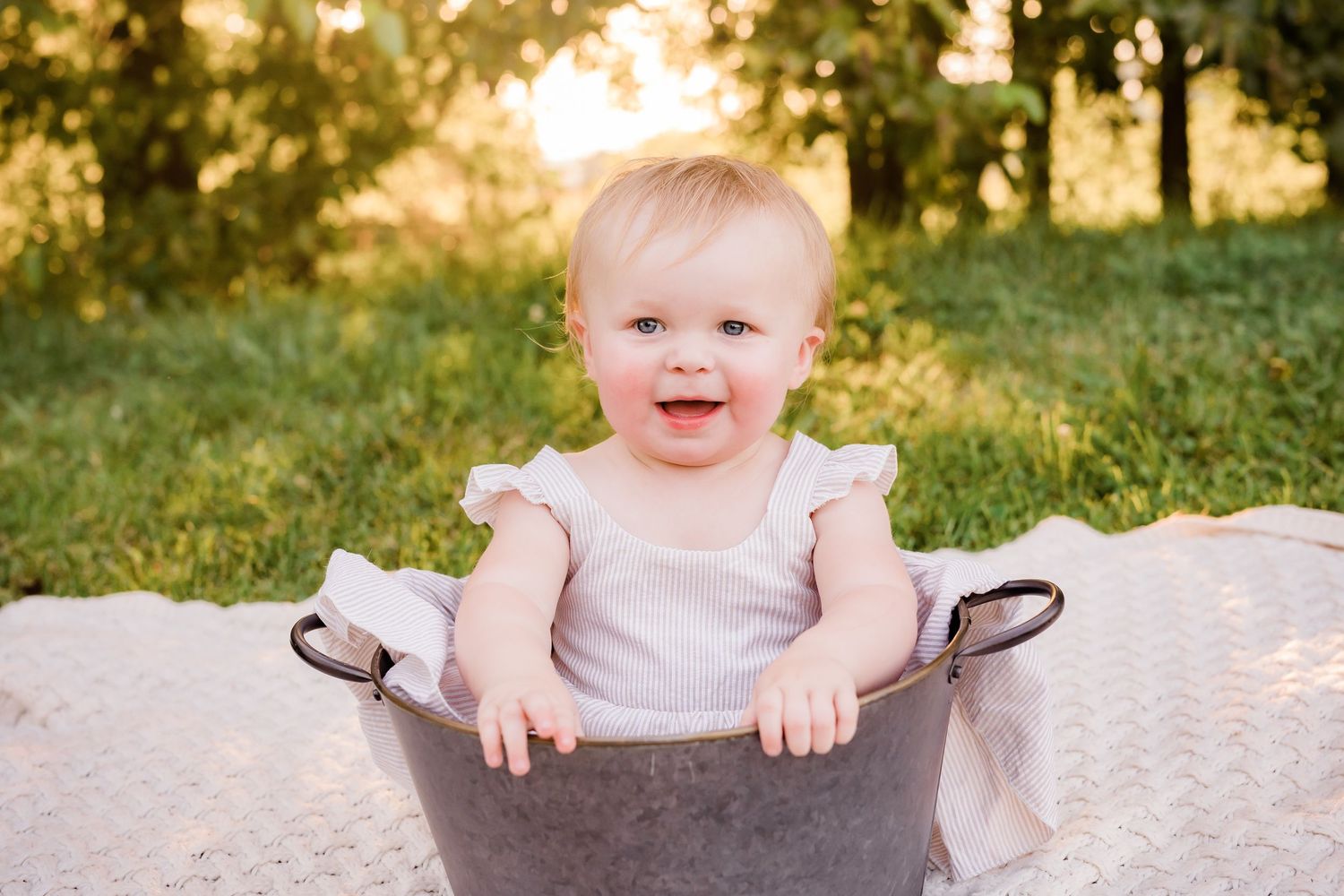 Happy smiling baby girl sitting in a vintage metal tub outdoors in golden sunlight.