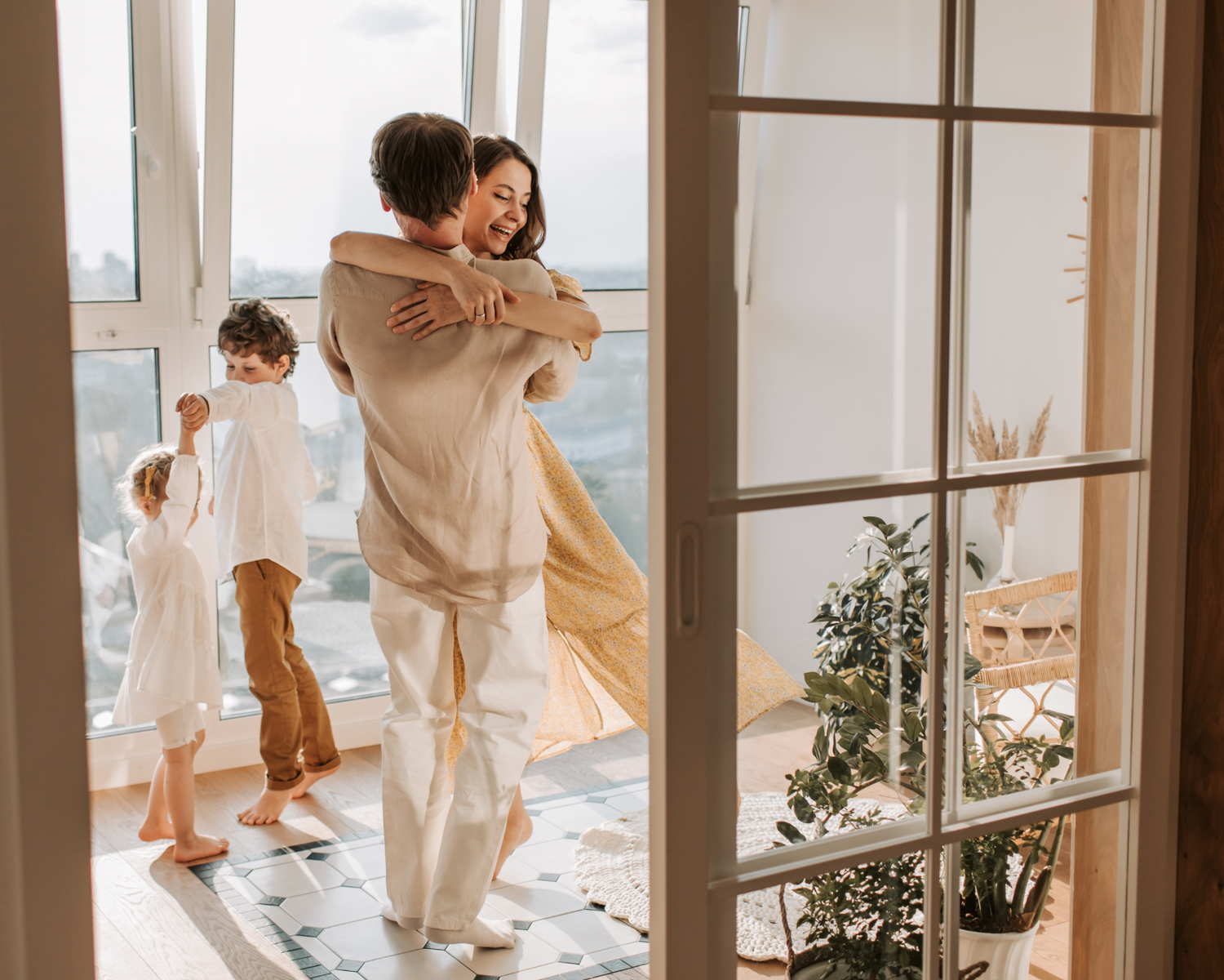 Family silhouettes dancing together near large windows on a bright sunny day.