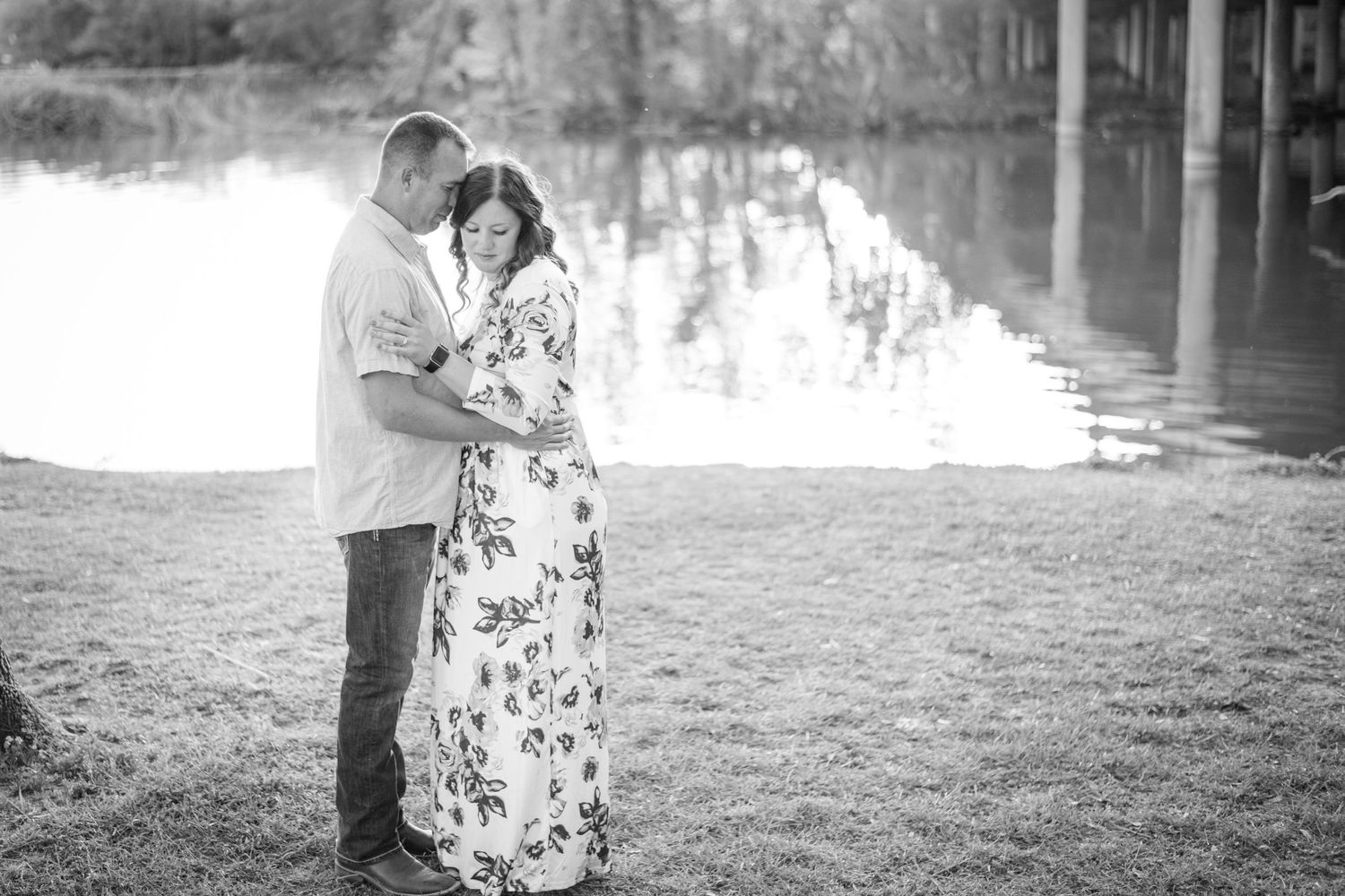 Black and white photo of a couple embracing by a reflective lake.