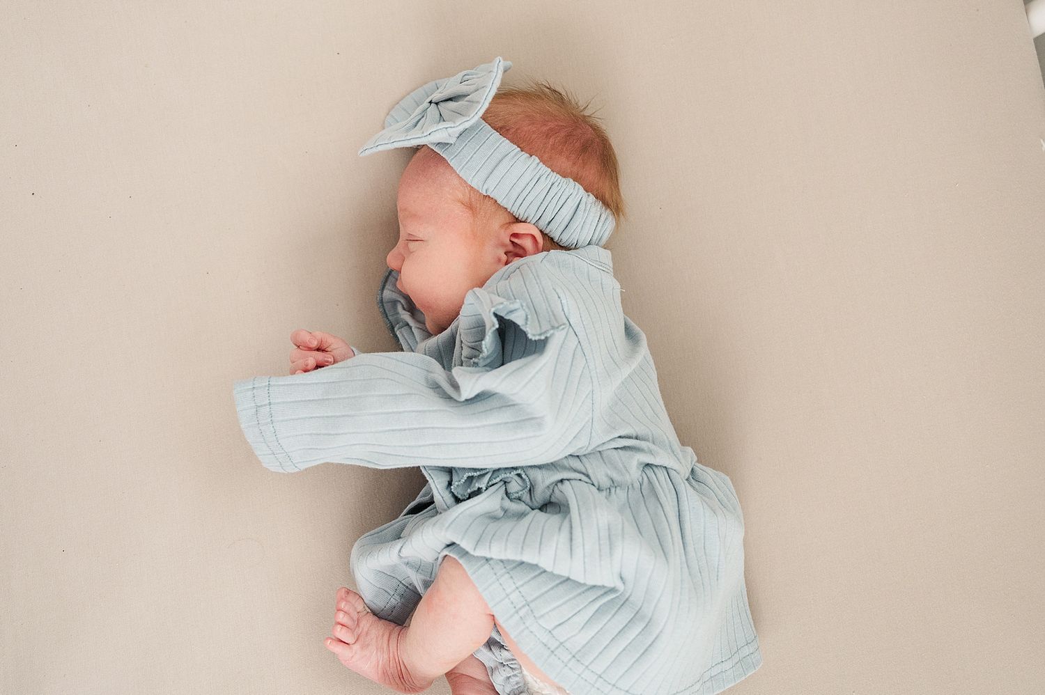 Sleeping newborn in soft blue outfit with matching headband lies on neutral background.