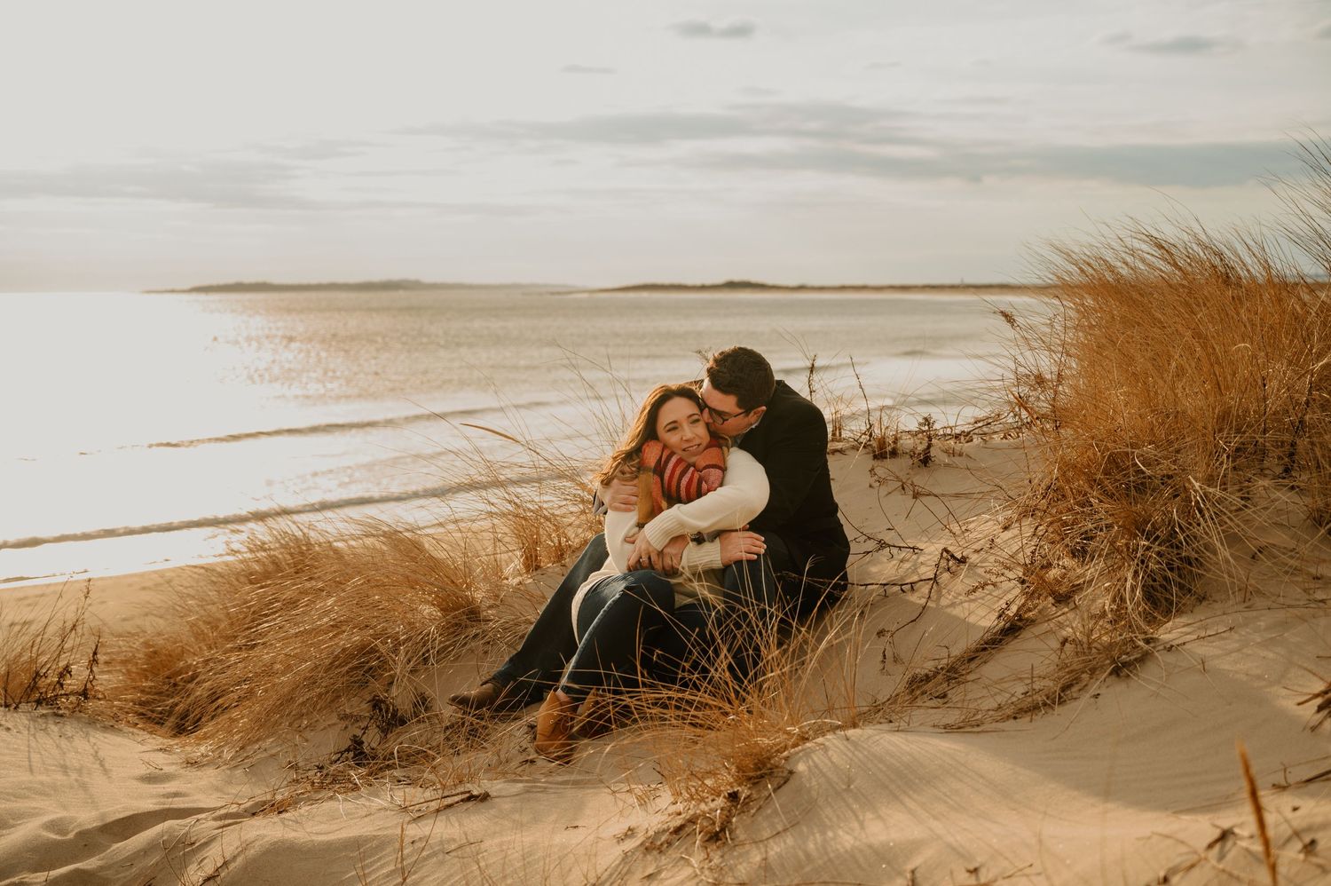 A couple shares an intimate moment on sandy beach dunes during golden hour.