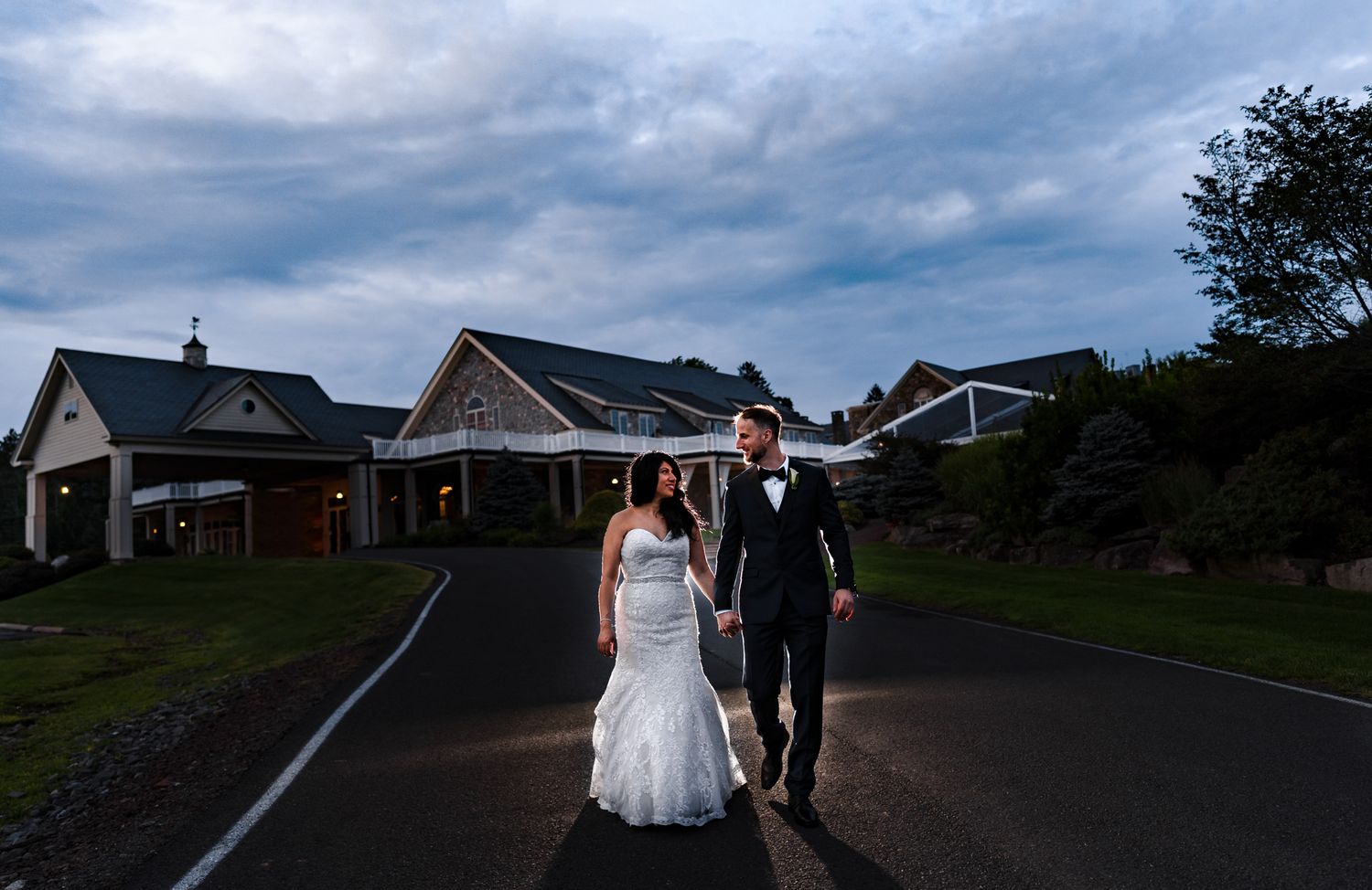 A couple walks down a suburban street at dusk with houses in the background.