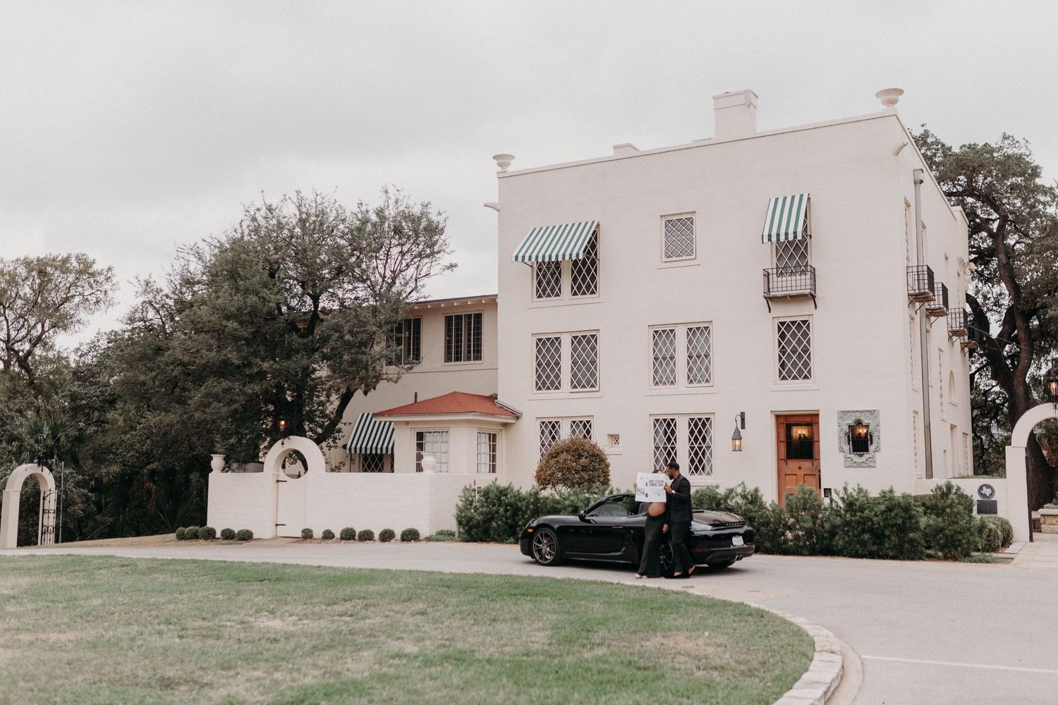 White Mediterranean-style mansion with striped awnings and lush landscaping.