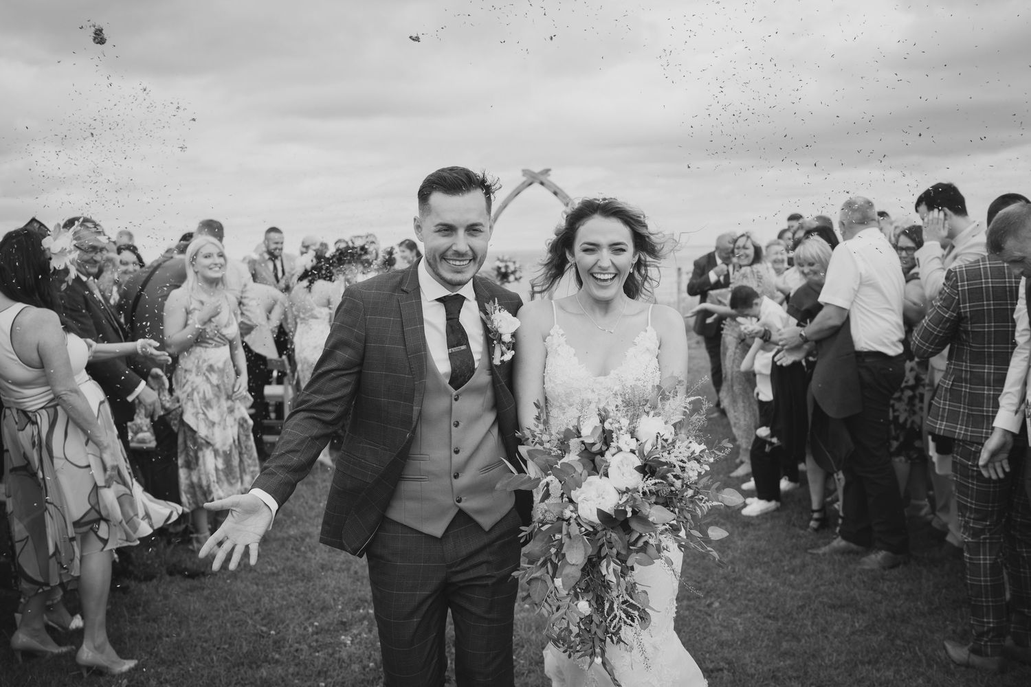 A joyful wedding celebration with guests throwing confetti outdoors.
