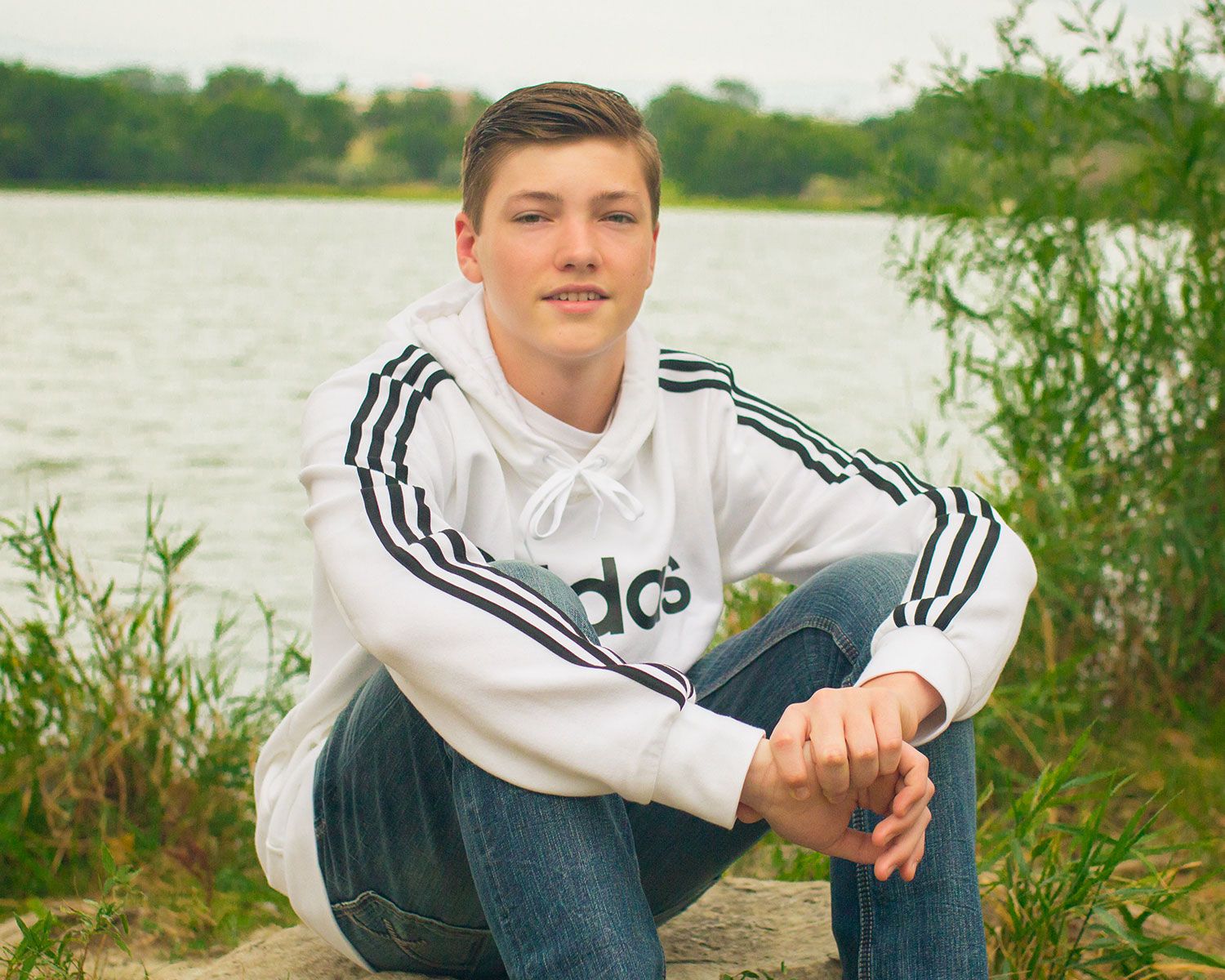 A casual outdoor portrait by a lake featuring someone in an Adidas sweatshirt.