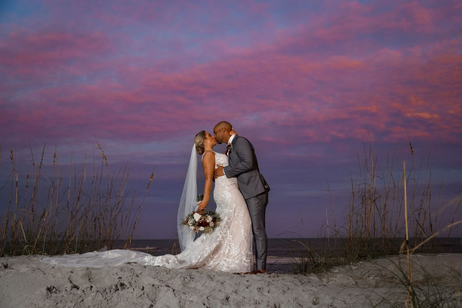 Couple shares intimate moment against dramatic sunset sky on sandy beach.
