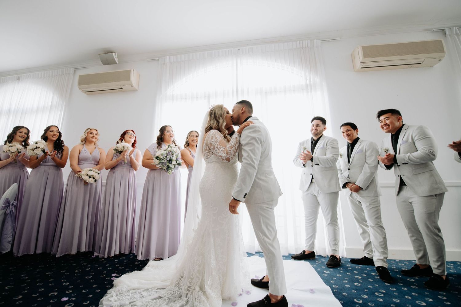 A wedding ceremony celebration with bridesmaids in purple dresses and groomsmen in light gray suits.