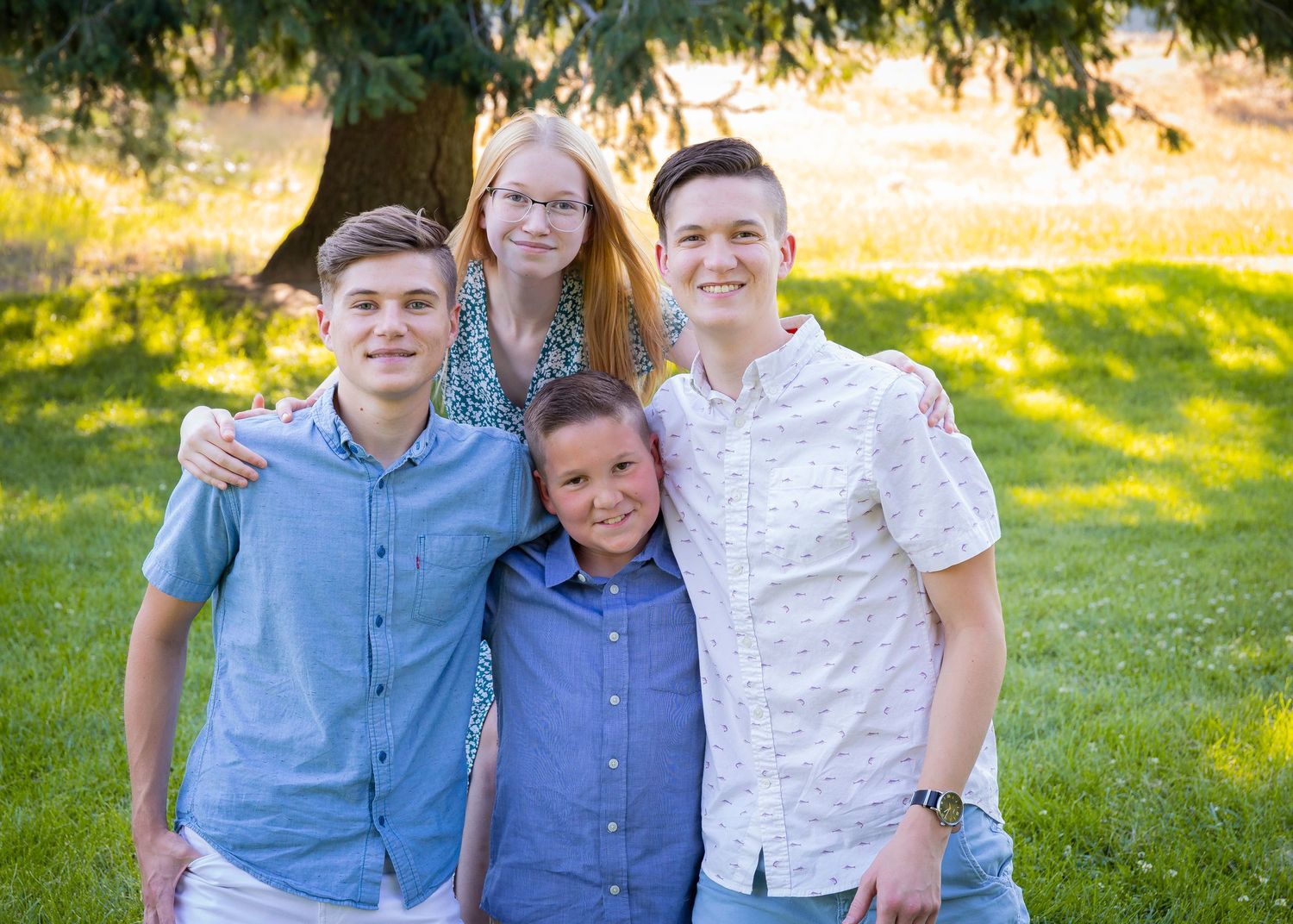 Family portrait of siblings outdoors in a sunny garden setting.