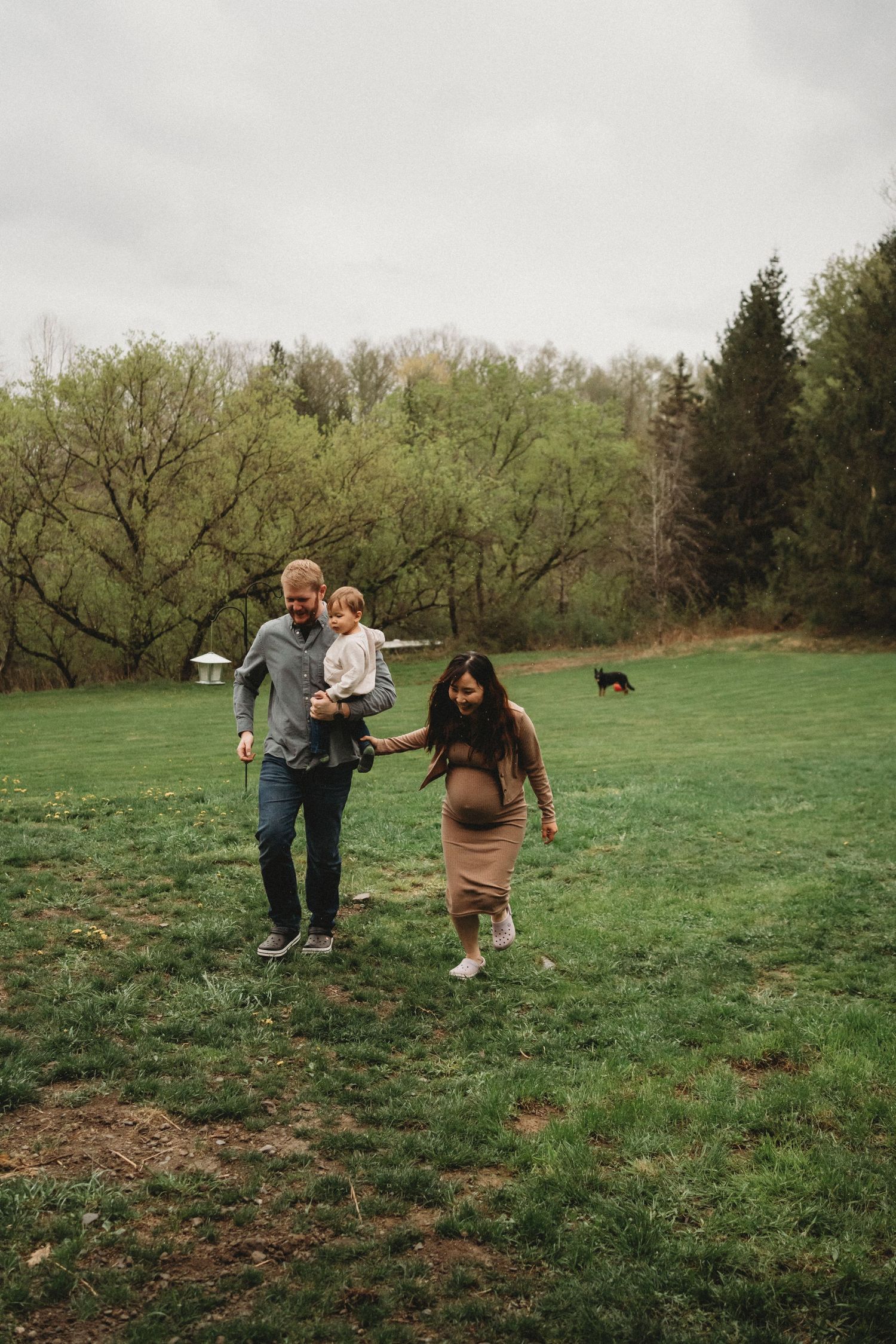 Family walking together across a green spring meadow with trees in the background.