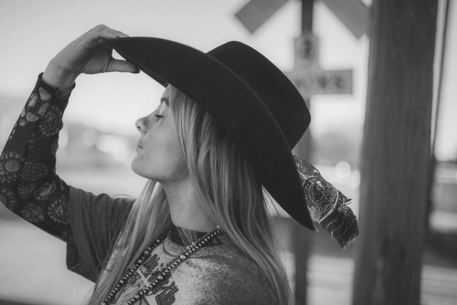 Black and white photo of person in wide brim hat looking up against blurred background.