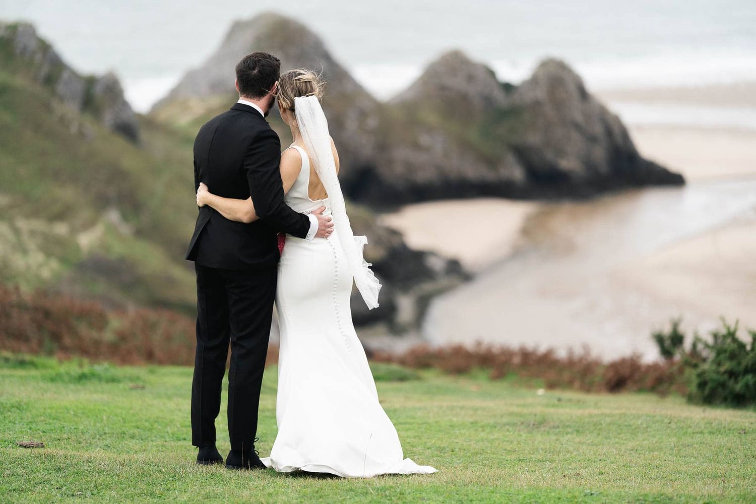 Bride and Groom arm-in-arm looking out to Swansea's Three Cliffs Bay