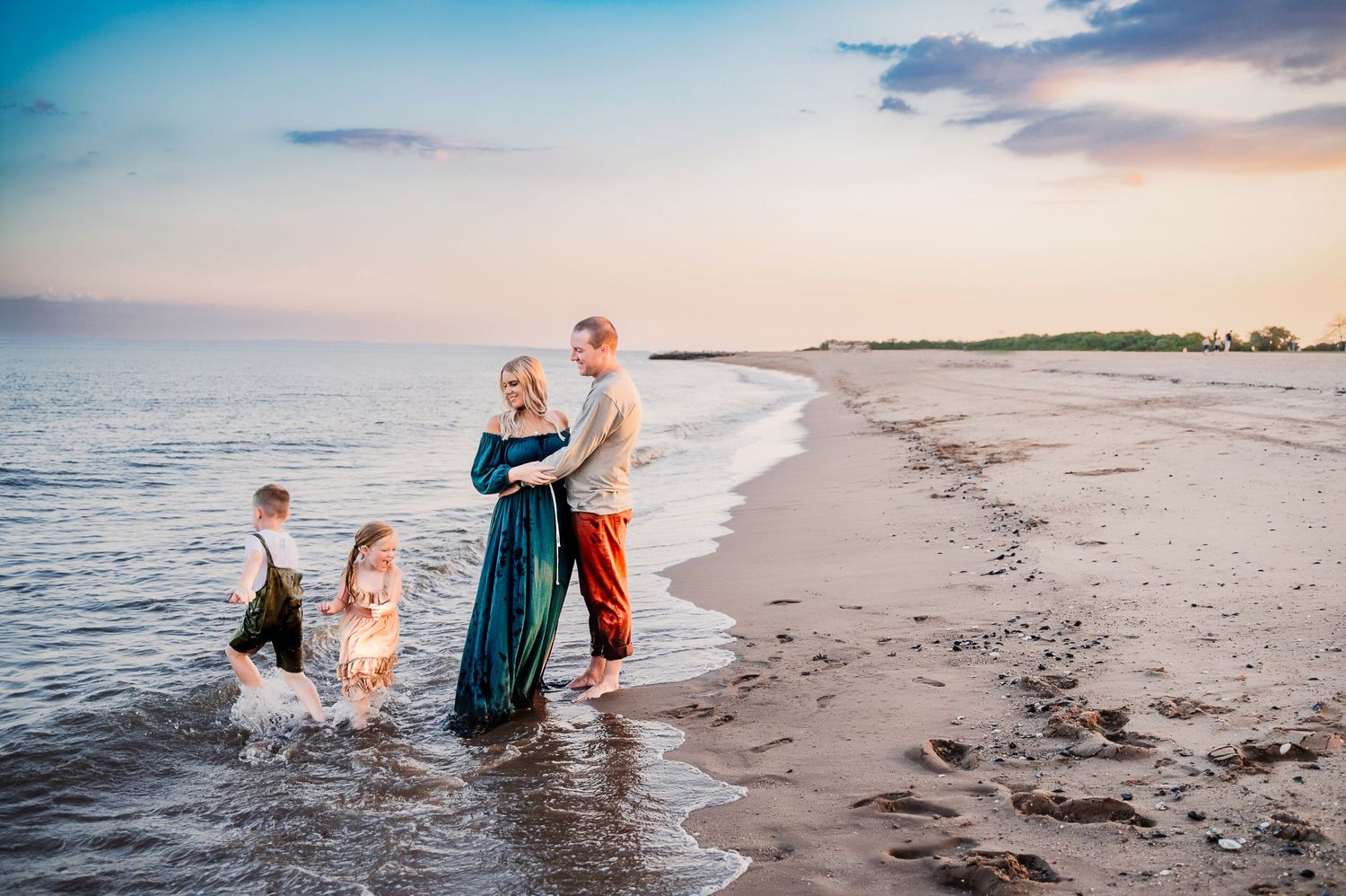 mother and father holding each other watching their two young children play on South Beach in Staten Island, NY