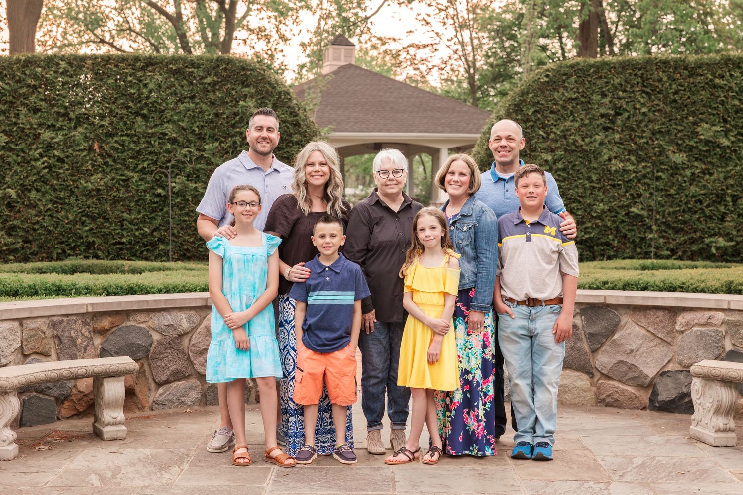 Multi-generational family portrait in front of garden wall with stone benches.
