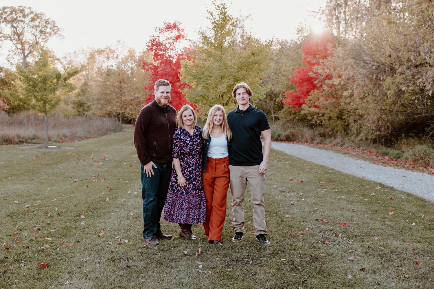 Group portrait outdoors with vibrant red fall foliage and walking path in background.