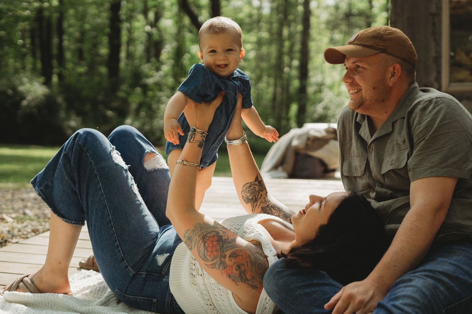 Playful outdoor family moment on a blanket enjoying quality time together in a wooded setting.