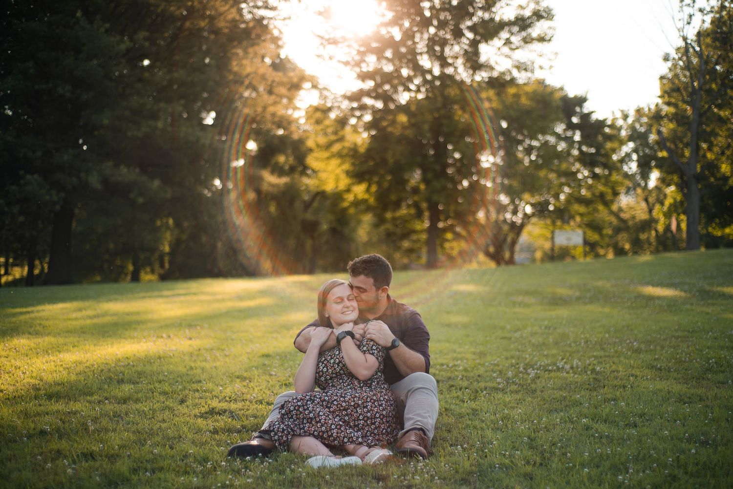 Romantic couple embracing on grassy hill during sunset in park.
