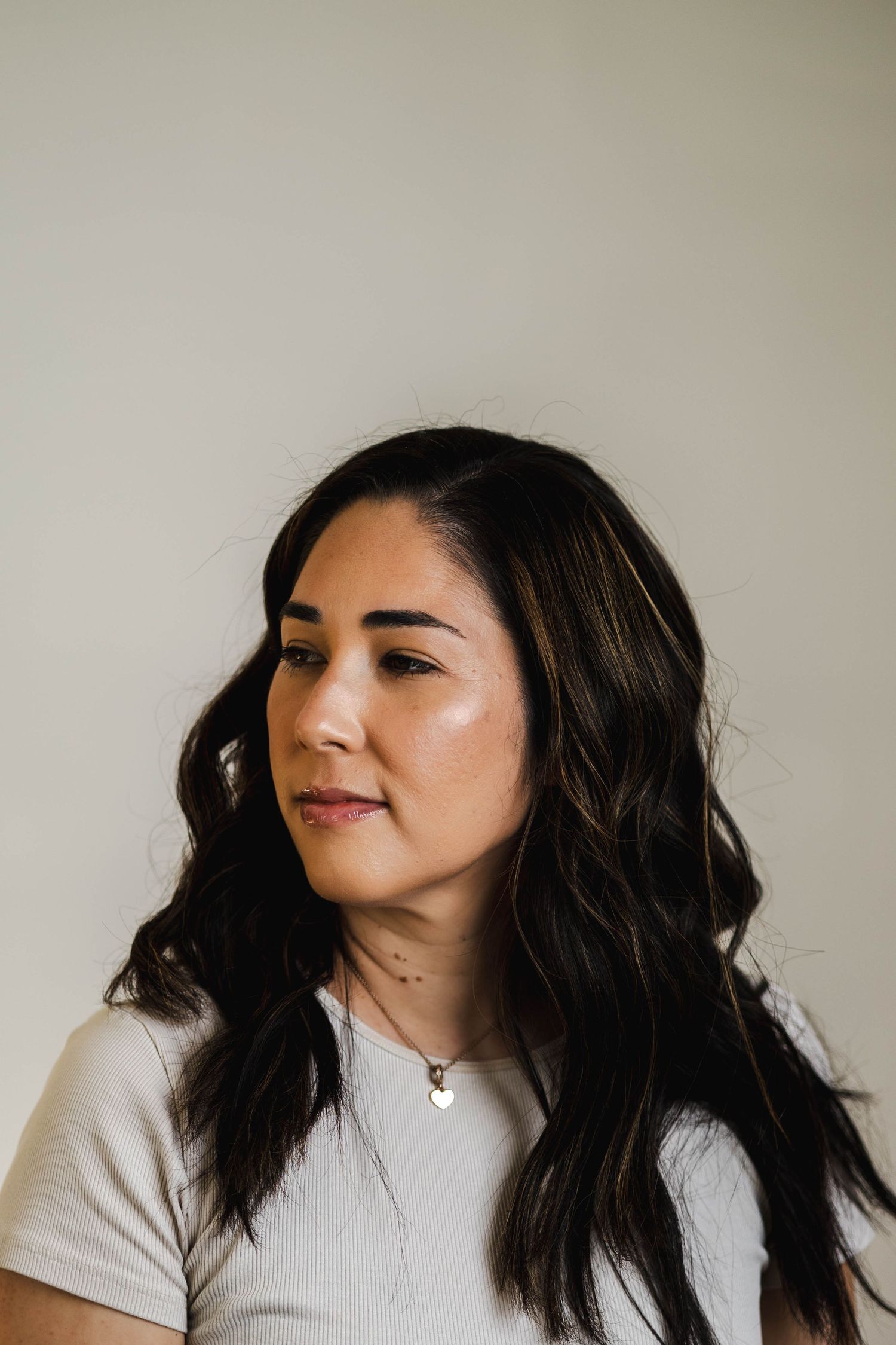 A profile portrait of a woman with long dark wavy hair wearing a light colored top.