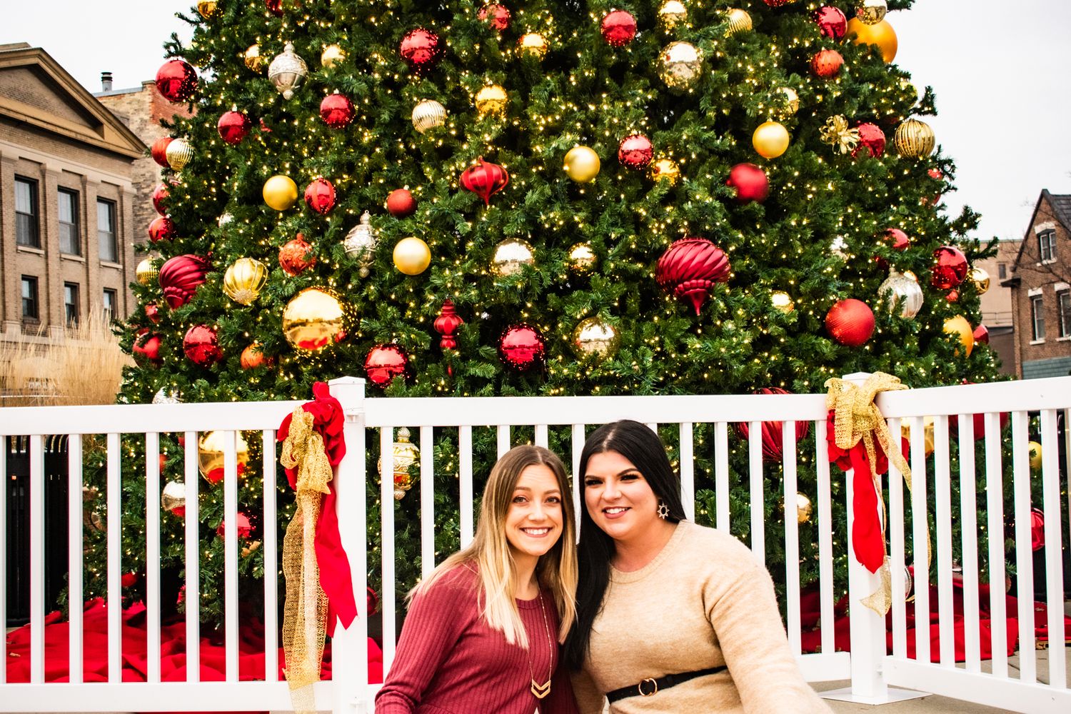Festive holiday scene with large Christmas tree decorated in red and gold ornaments behind white railing.
