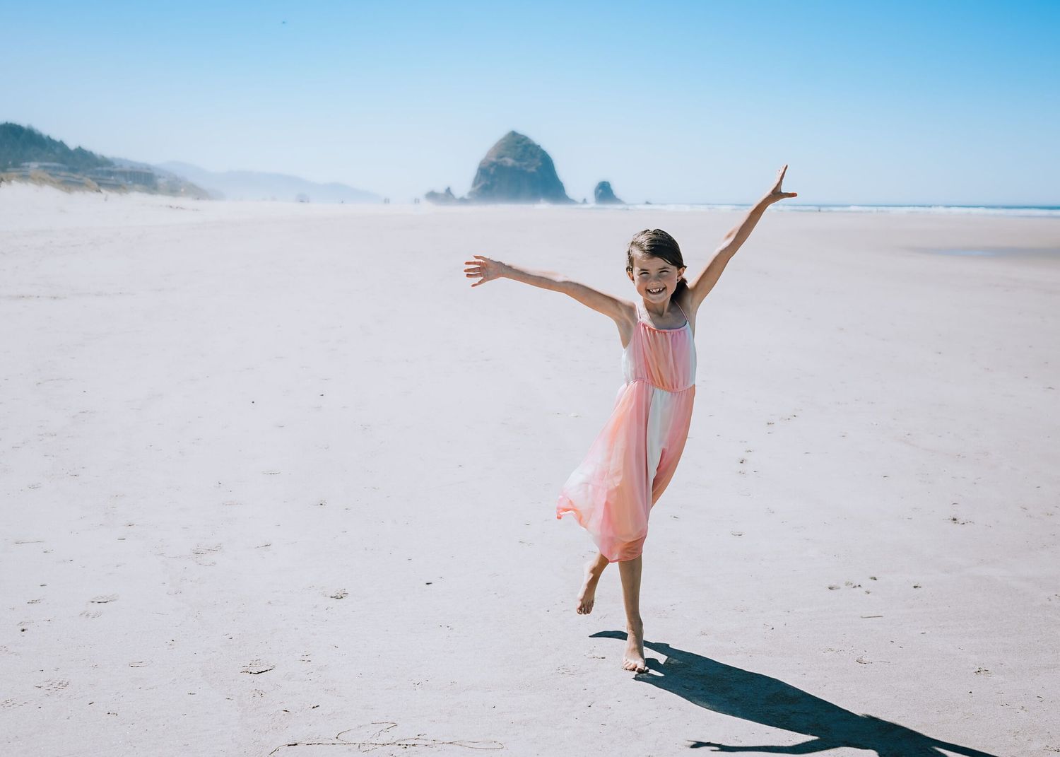 Dancing with joy on a sandy beach with Haystack Rock visible in the misty background.