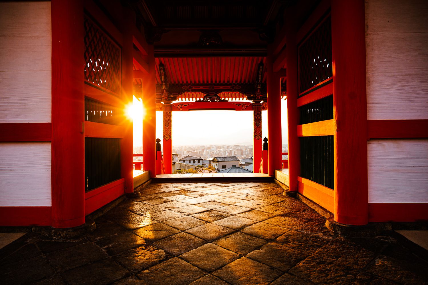 Red temple gateway framing sunset view over cityscape through traditional architecture.