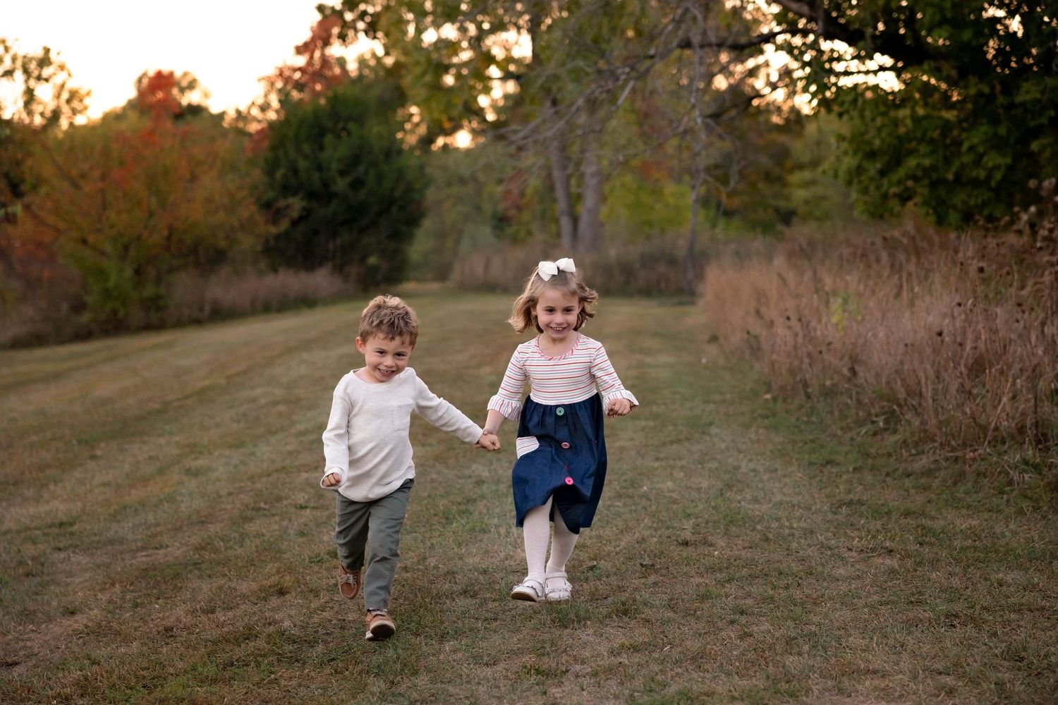 Two children run together down a grassy path during golden hour.
