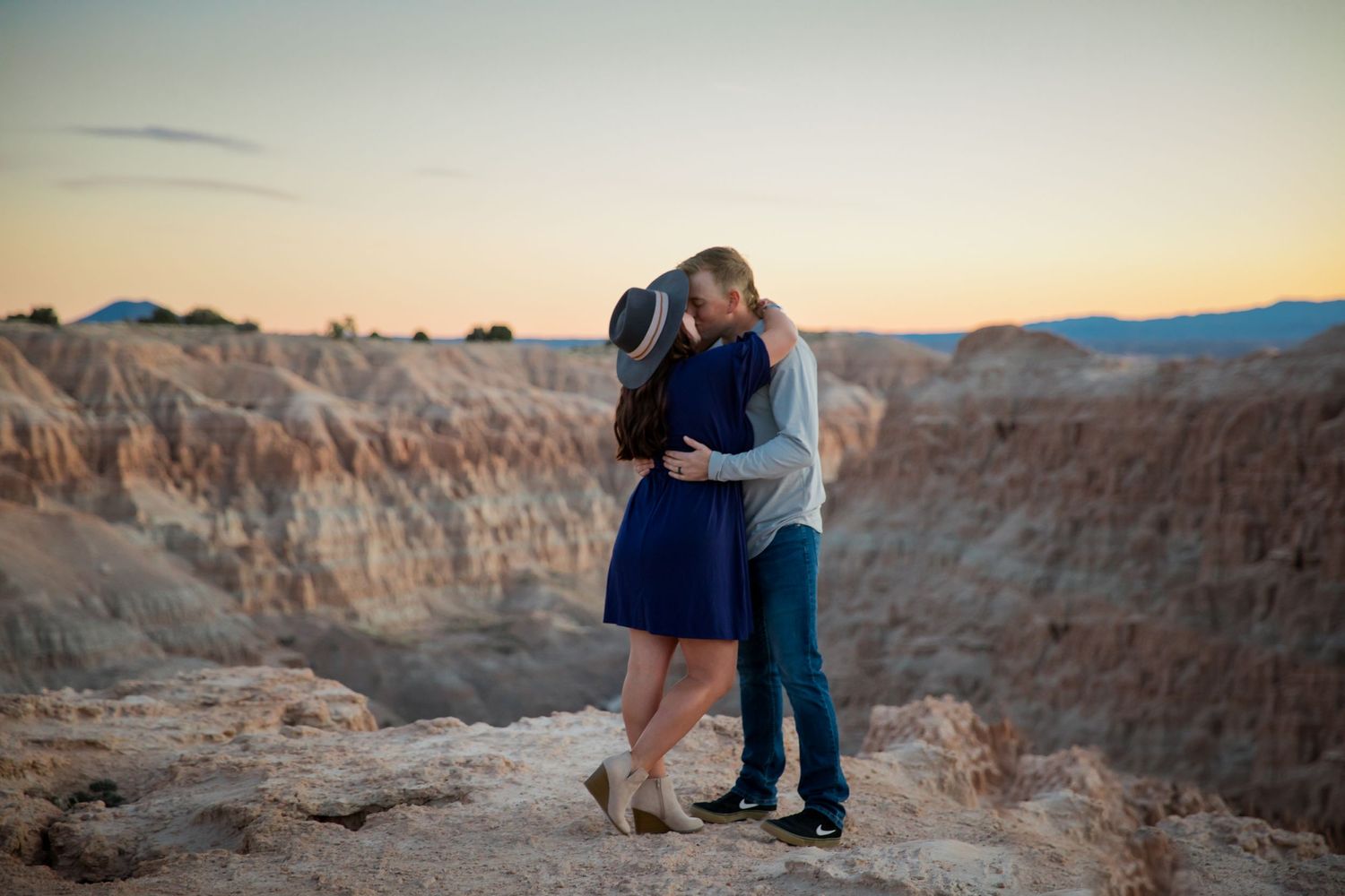 Couple embraces at sunset overlooking dramatic desert canyon landscape.