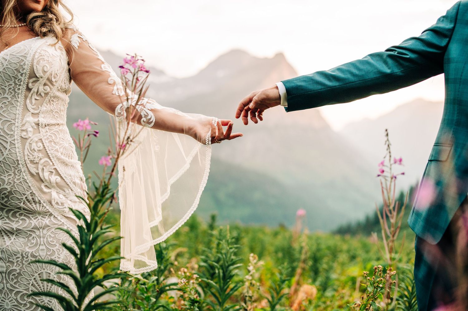 Couple holding hands in a wildflower meadow with mountain peaks in the background.