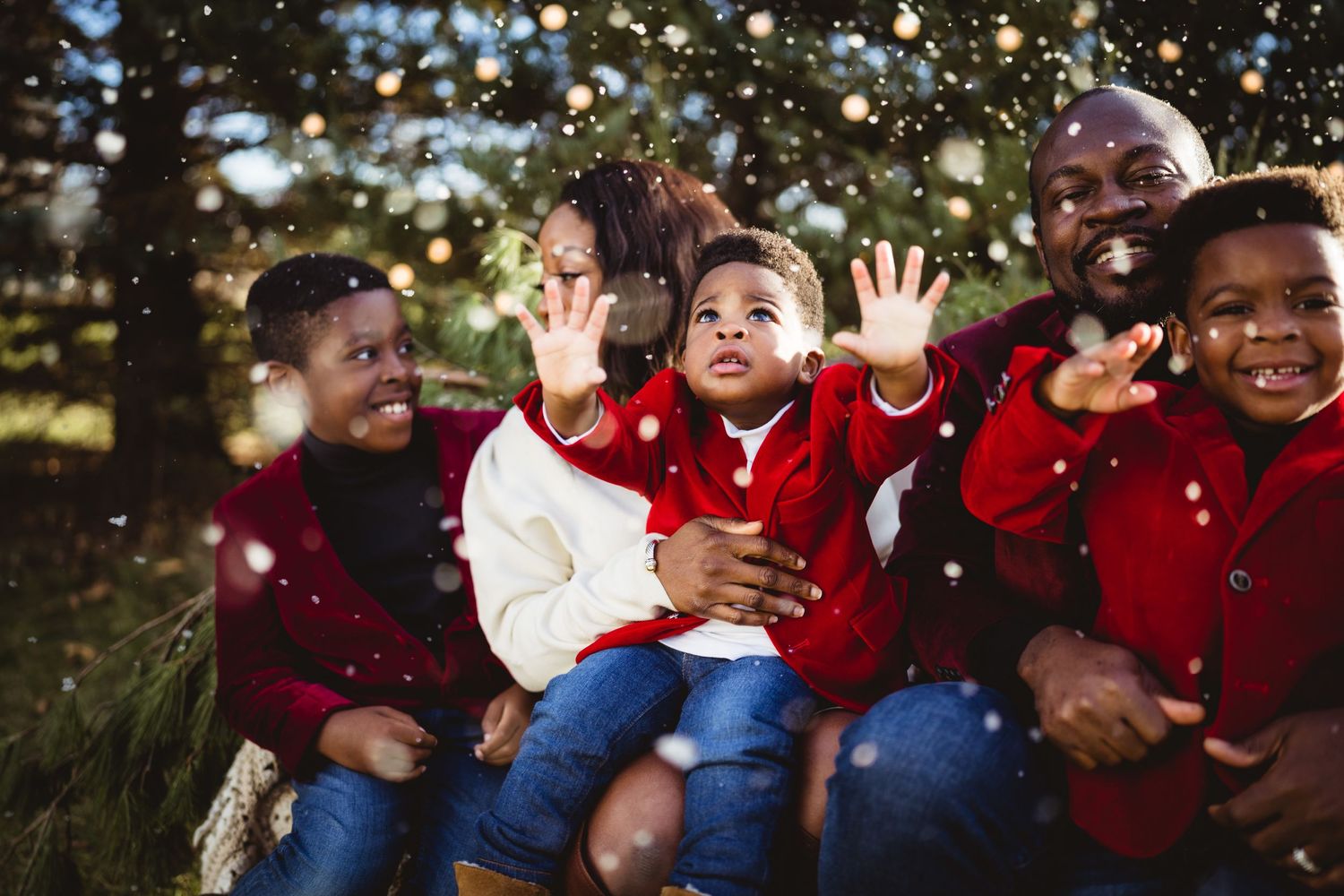 Children sitting together outdoors laughing with snow falling around them.