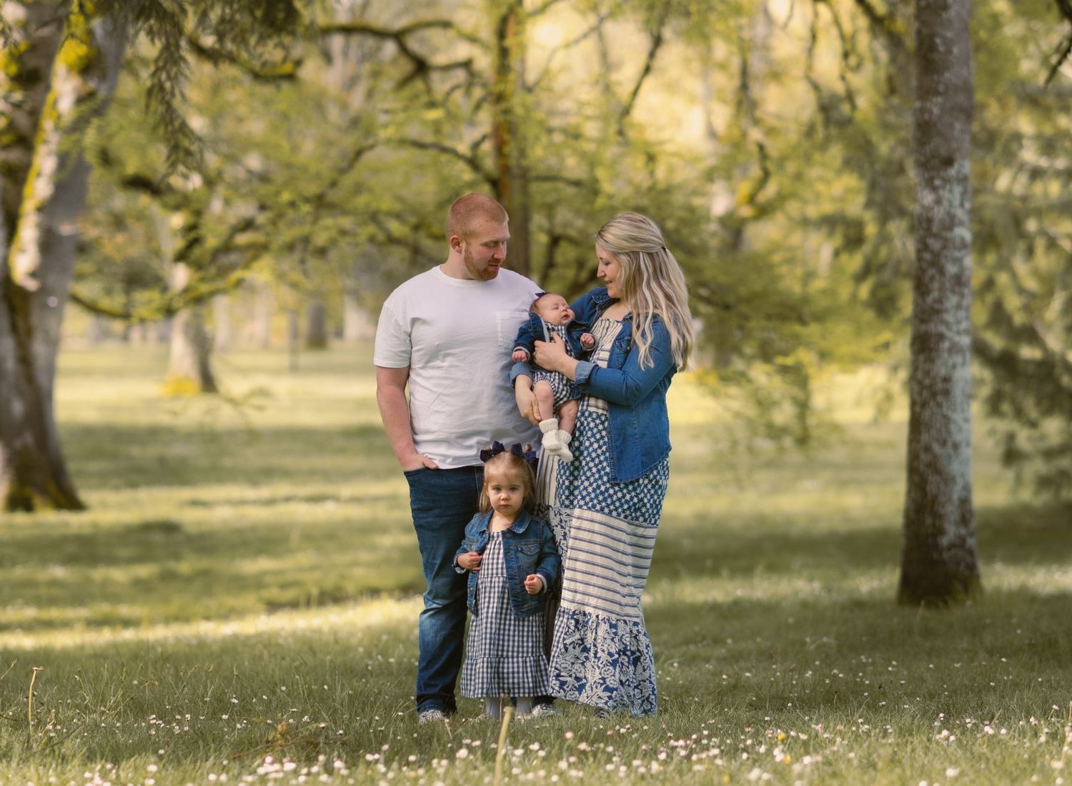 A beautiful family of four posing standing up in a forest area. Sunny and bright.