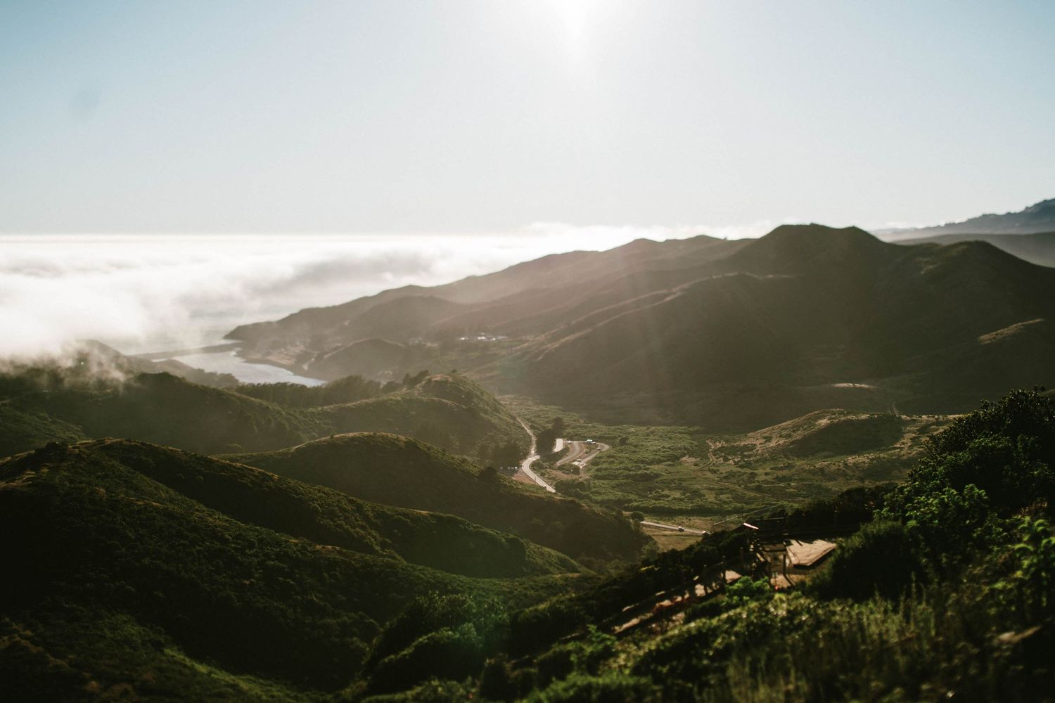 Rolling hills descend into fog-covered valleys under bright sunlight.