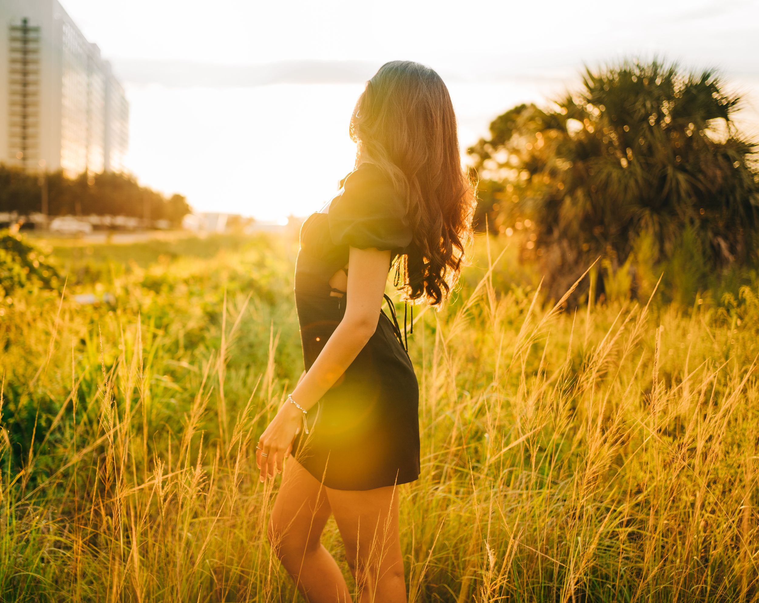 Silhouette in short dress standing among tall grass at golden hour.