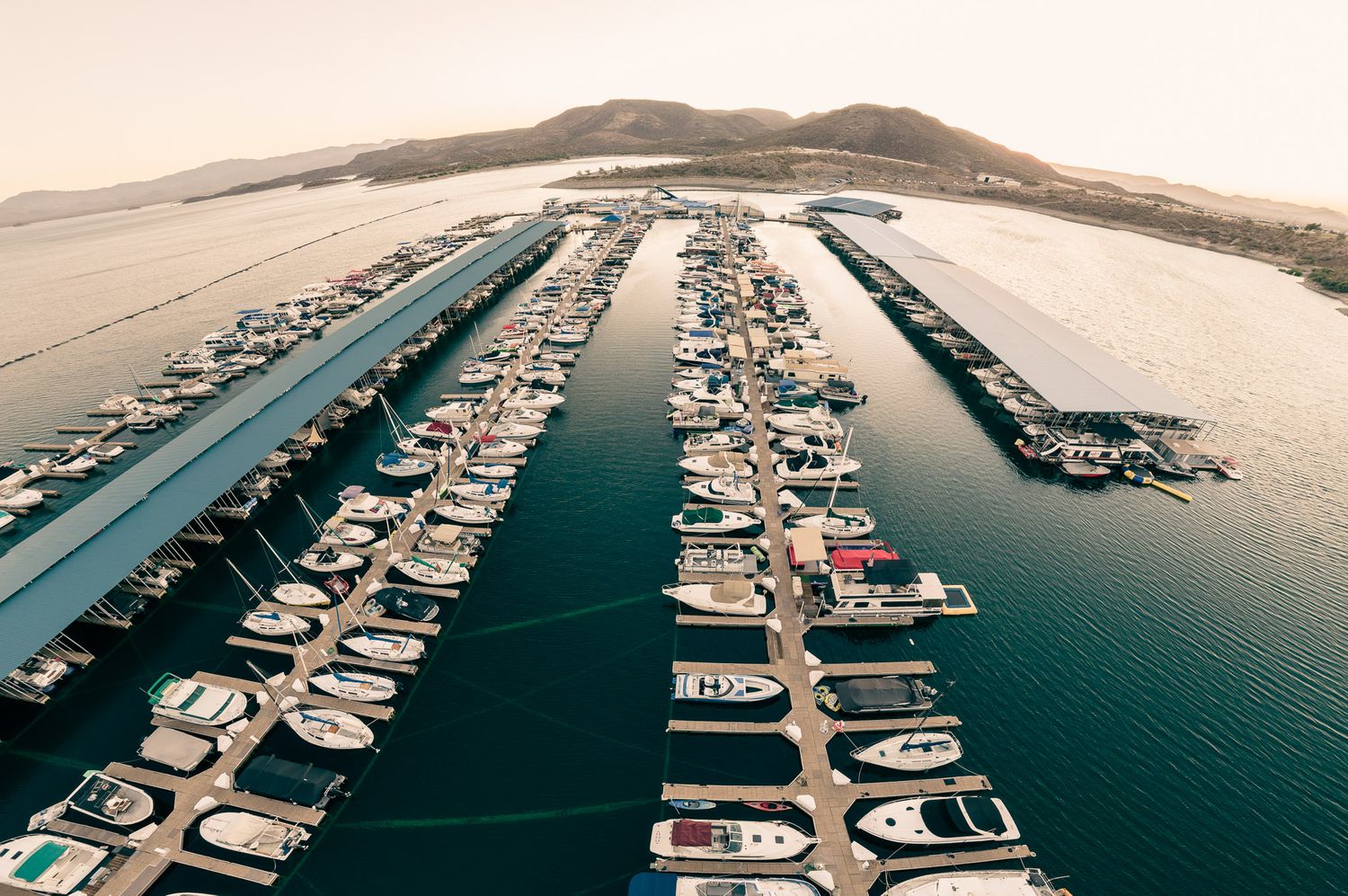 Aerial view of a marina with rows of boats docked in calm waters during sunset.