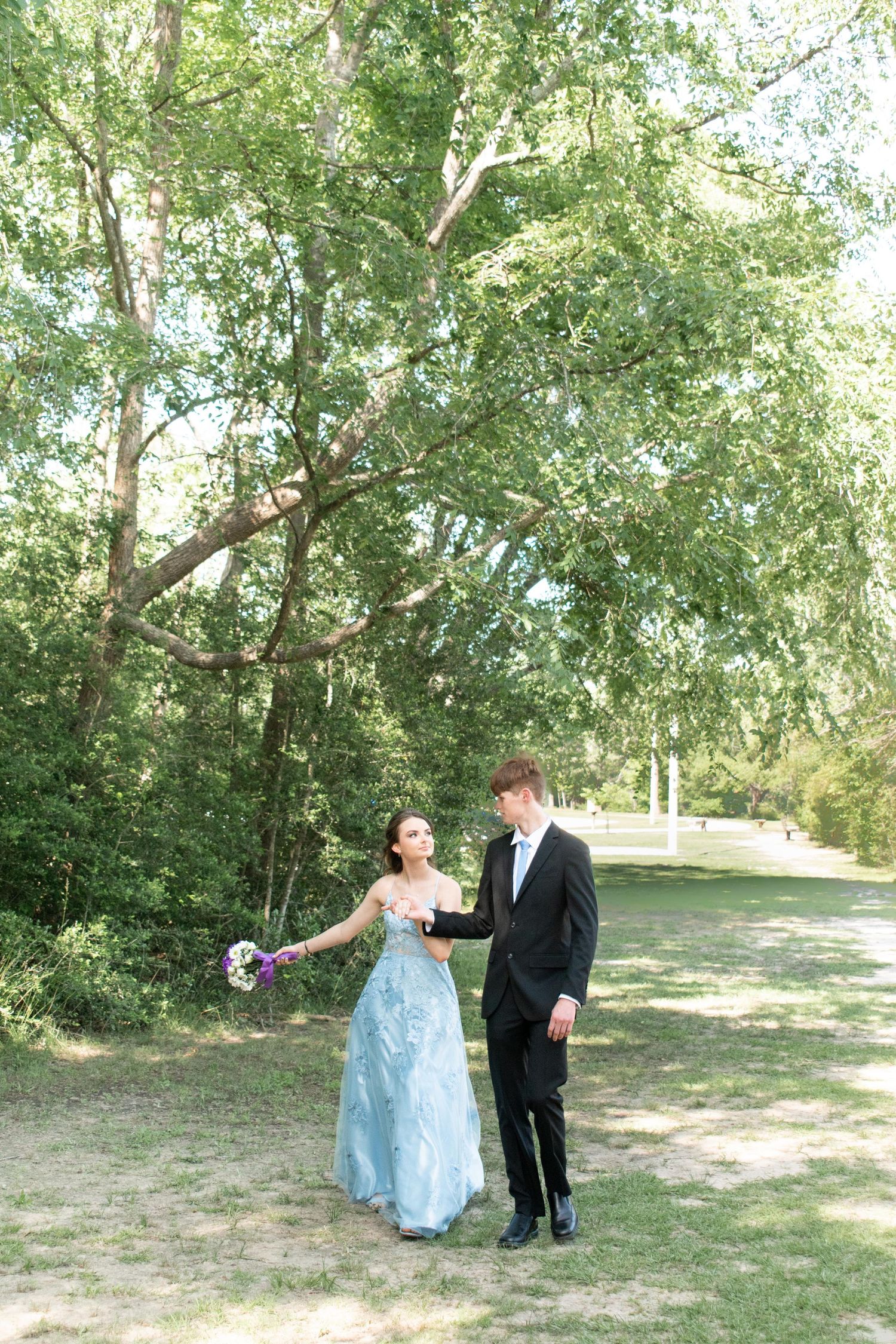 Couple in formal wear having romantic moment on woodland path with trees in background.